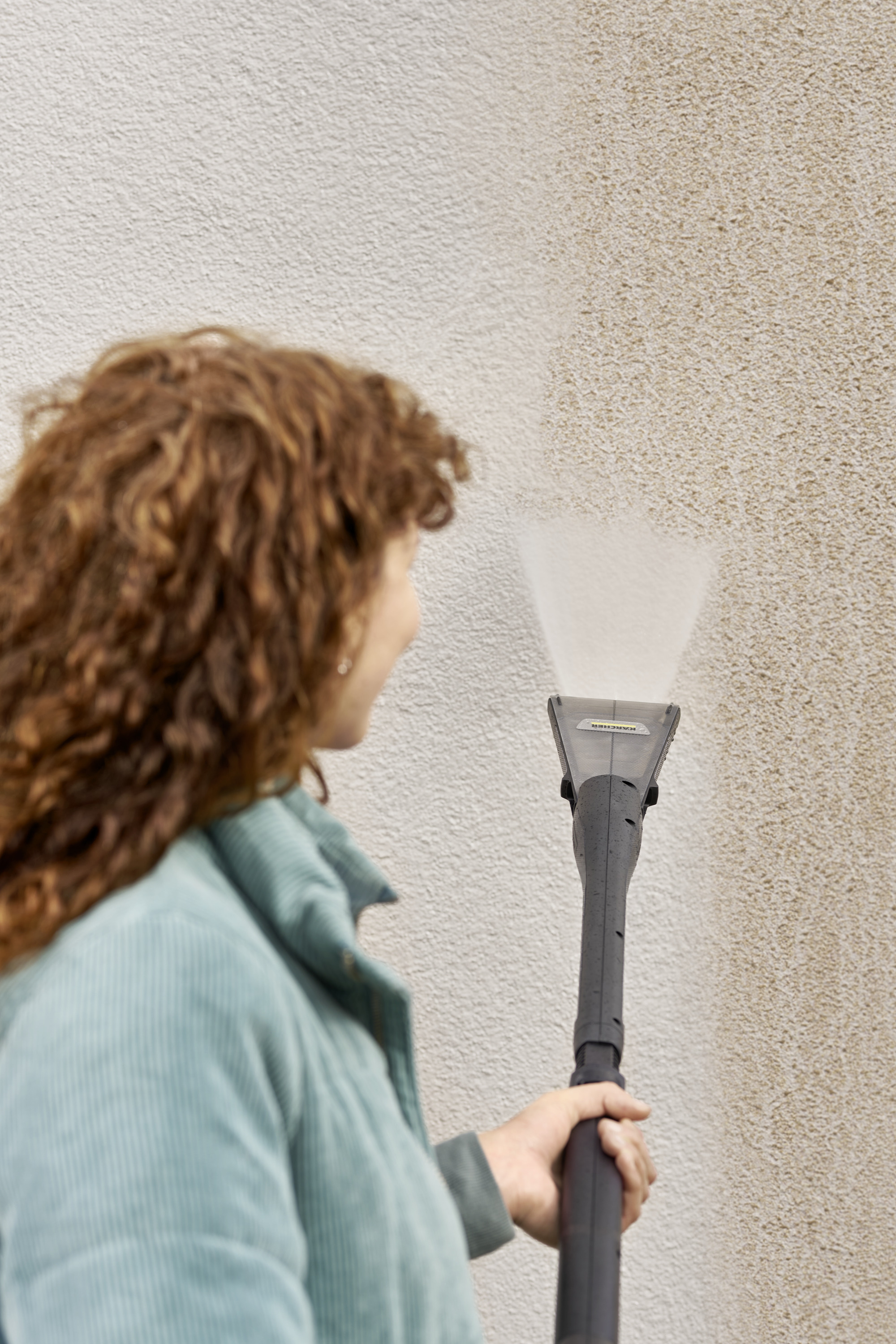Kobieta czyszcząca ścianę myjką ciśnieniową.