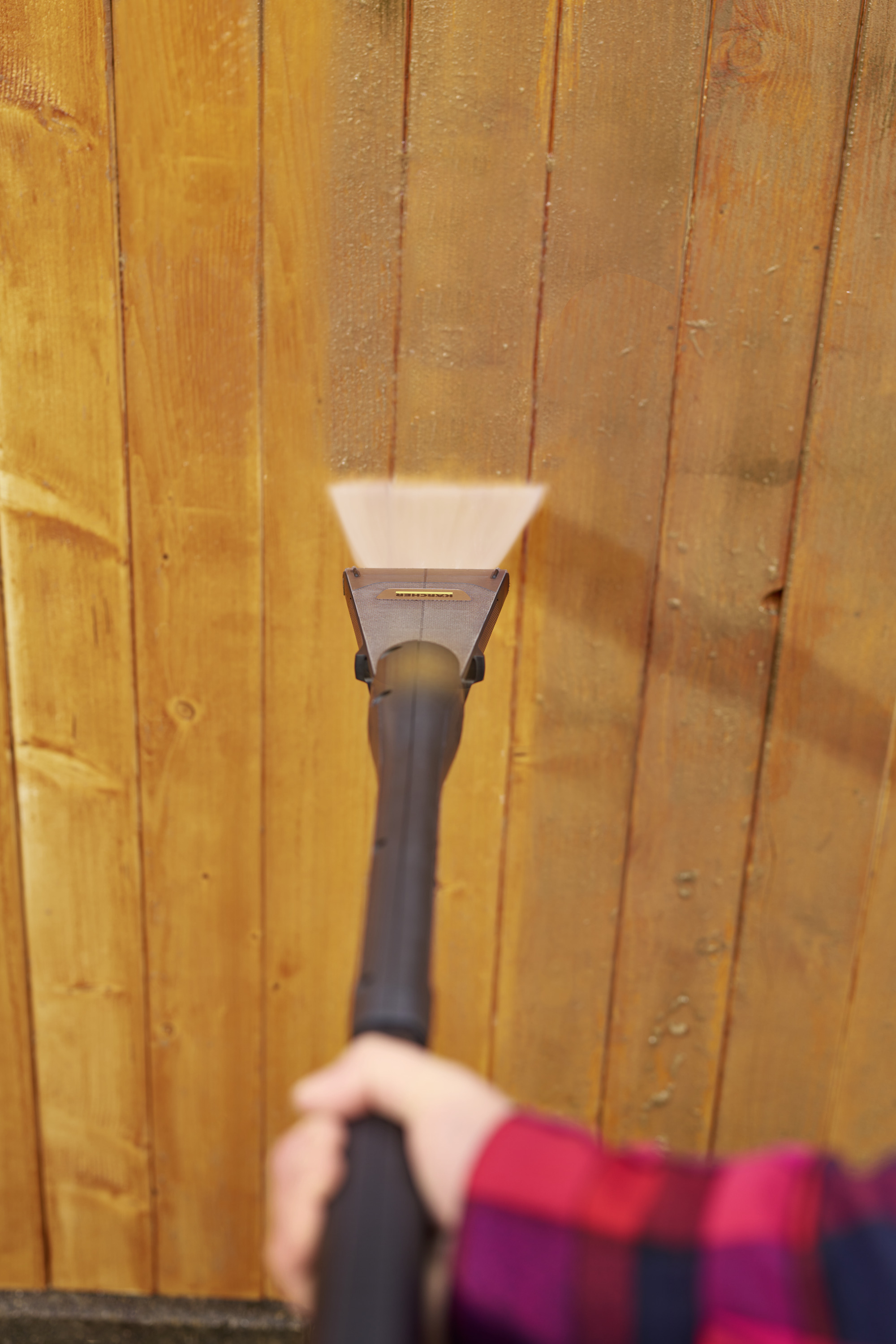 Osoba czyszcząca drewnianą ścianę myjką ciśnieniową.