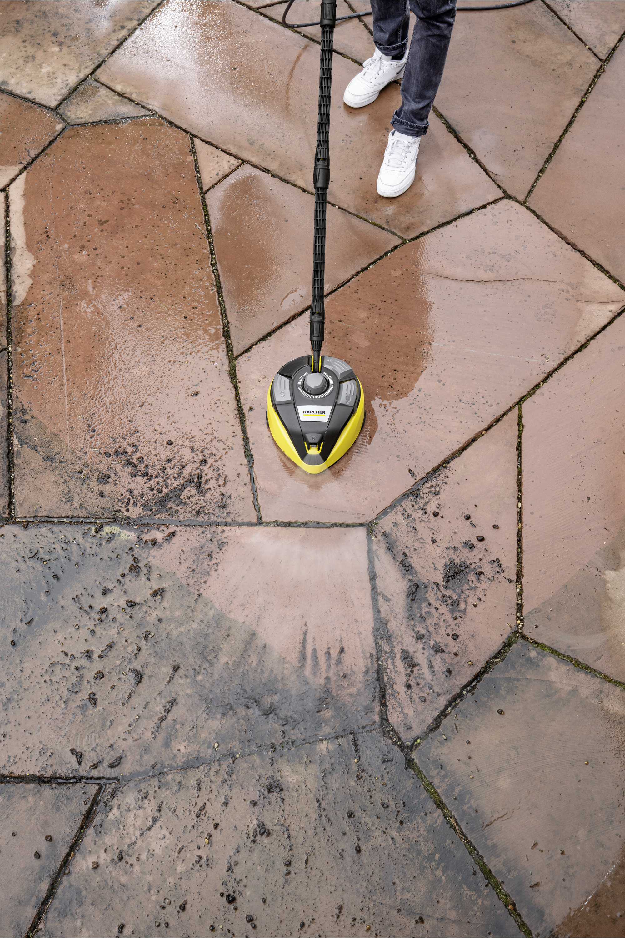 Osoba czyszcząca czerwonobrązową kamienną podłogę żółto-czarnym urządzeniem Kärcher.