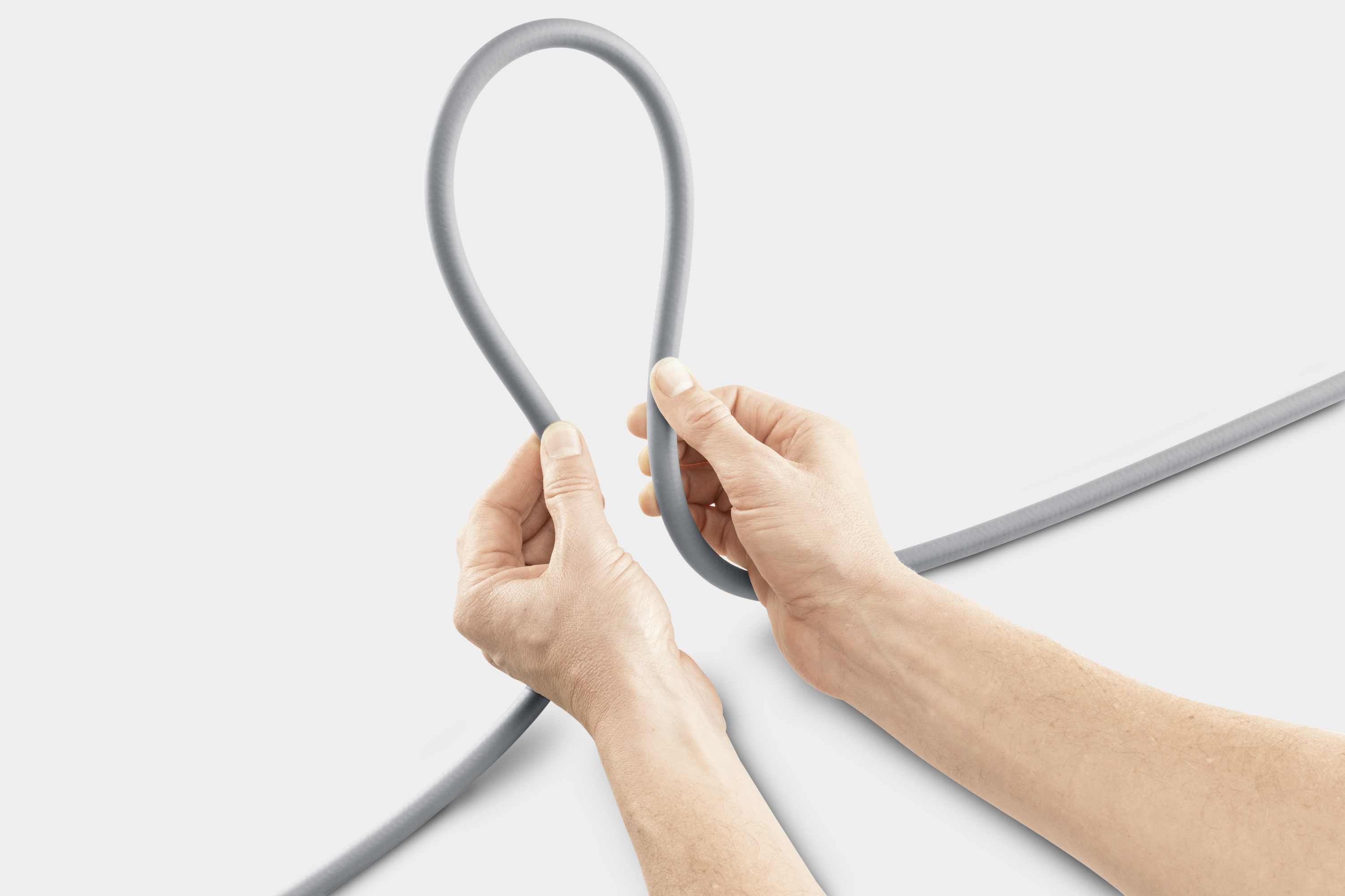 Dłonie formują pętlę z szarym kablem na białym tle.