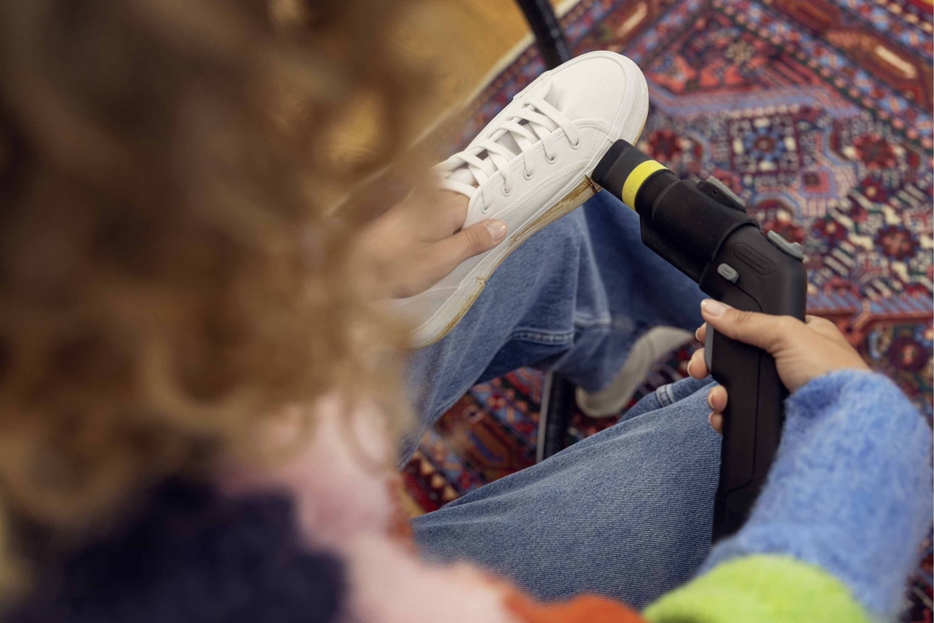Osoba czyszcząca białe buty za pomocą urządzenia czyszczącego. Osoba siedzi na dywanie.