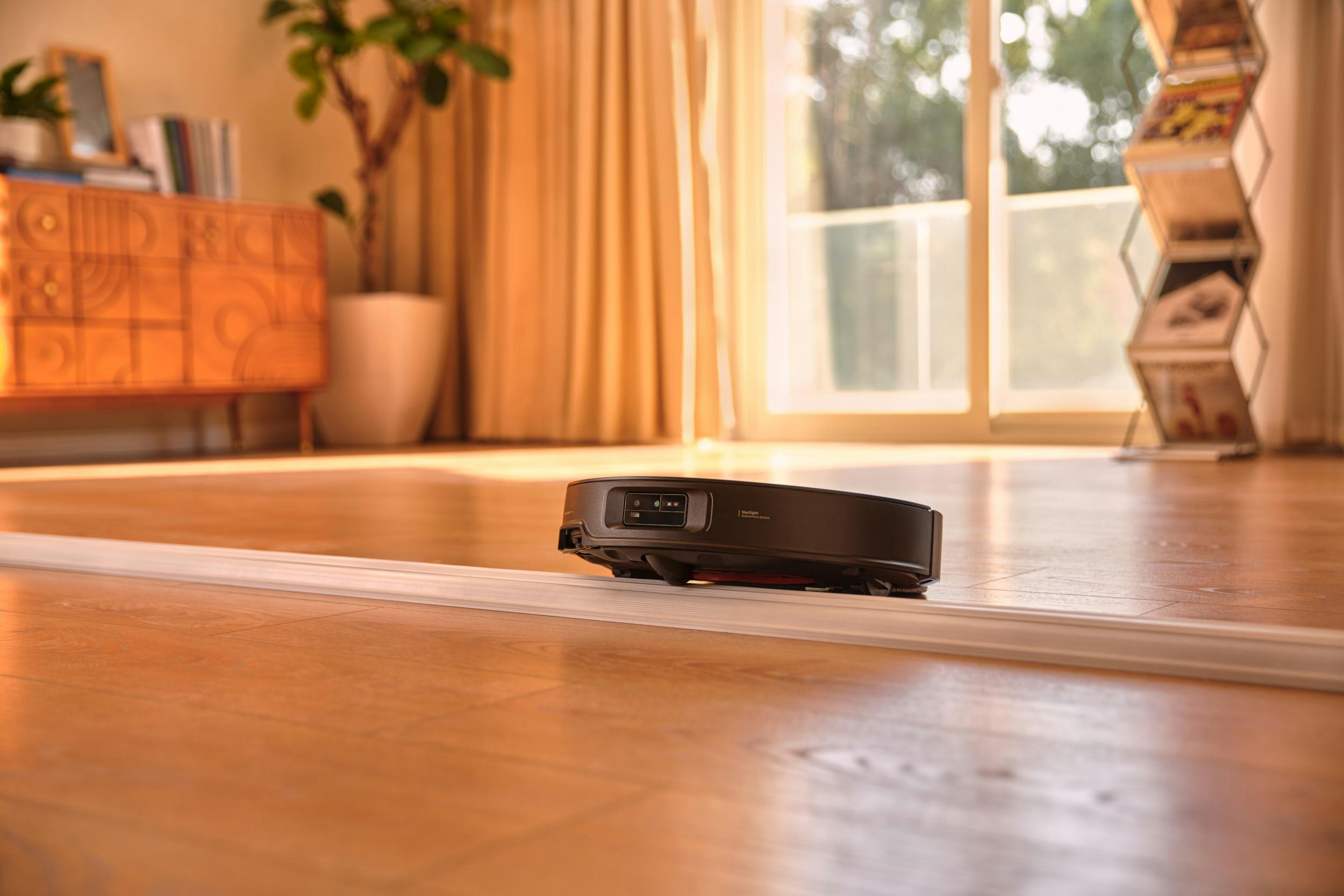 Ein schwarzer Roboter-Staubsauger fährt über eine Schiene auf einem Holzboden.