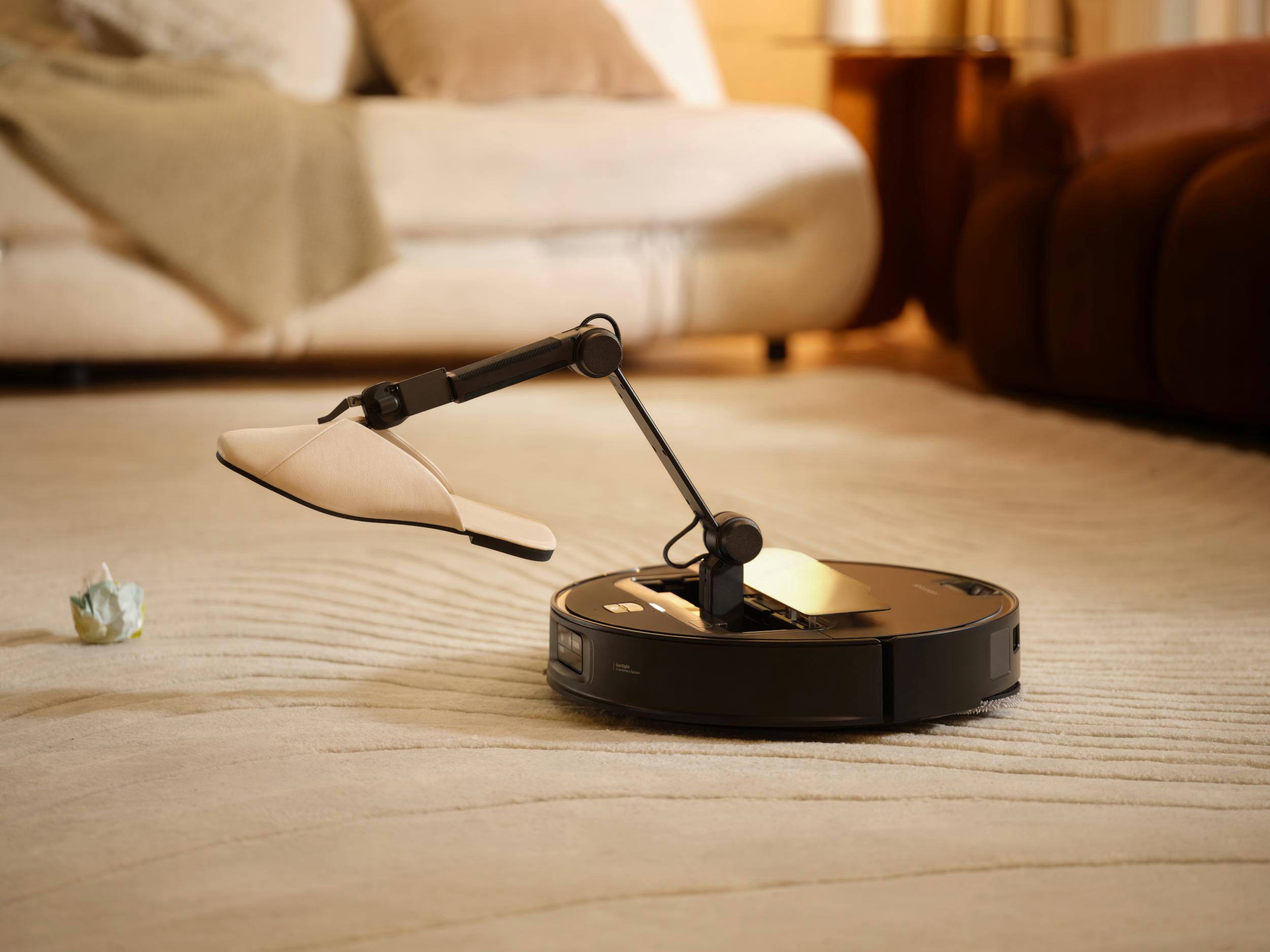 Ein Roboter-Staubsauger mit einem Arm, der einen Pantoffel hält, auf einem Teppich.