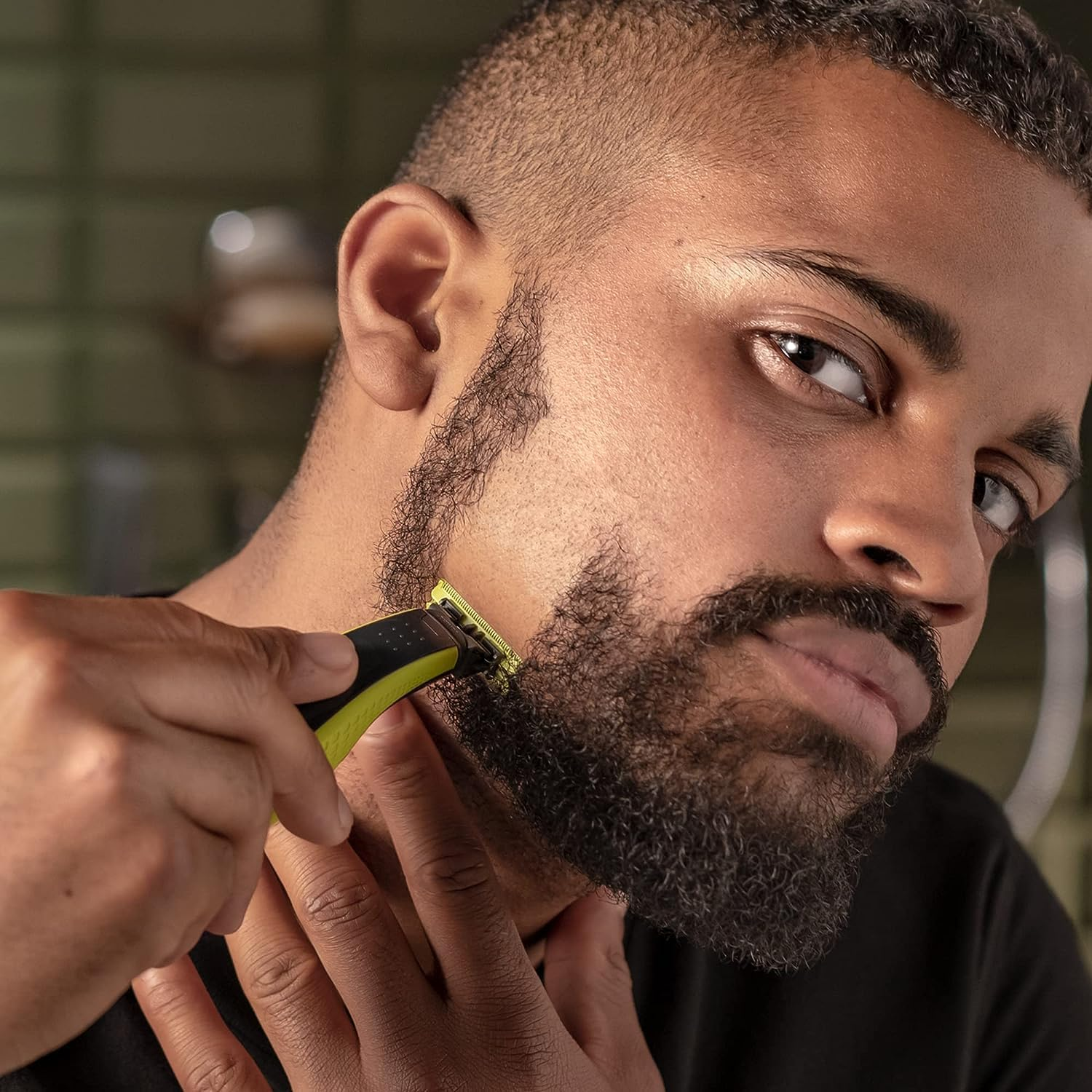 Un hombre se afeita la barba con una afeitadora verde, primer plano de su rostro.