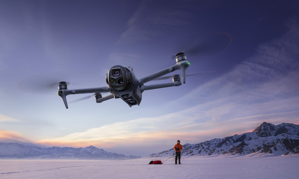 Dron lecący nad zaśnieżonym krajobrazem, z osobą ciągnącą sanki.