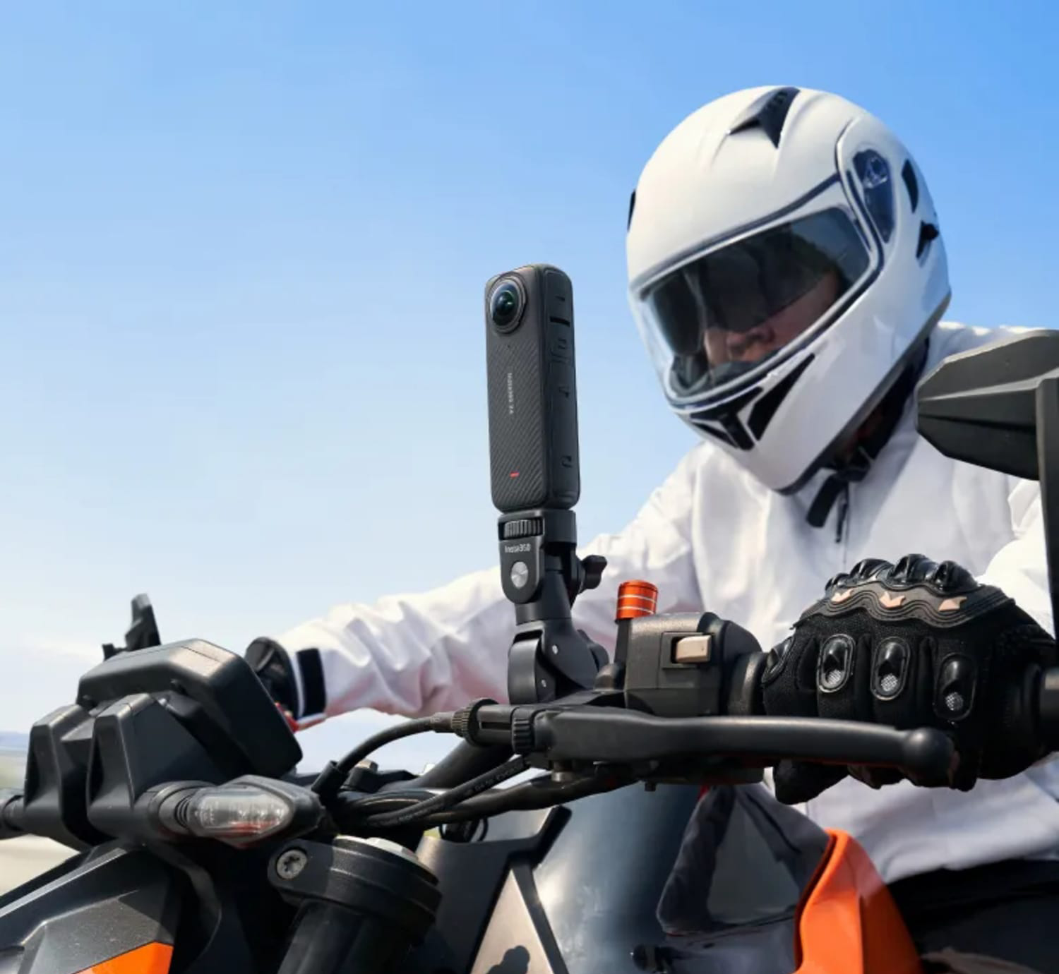Motoros sisakkal és a kormányra szerelt kamerával, kék égbolt előtt.