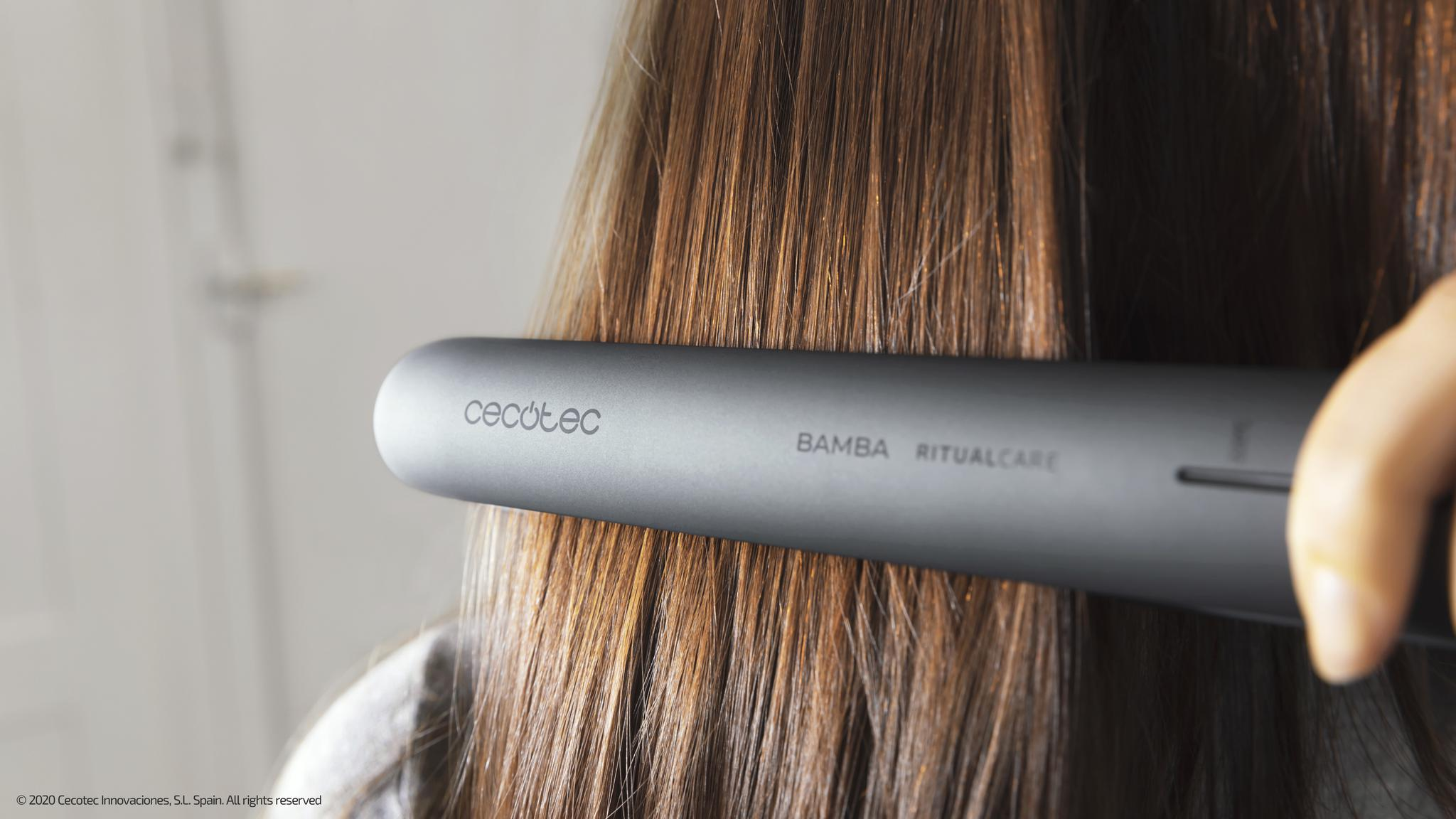 Szara prostownica prostuje włosy osoby. Tło jest rozmyte.