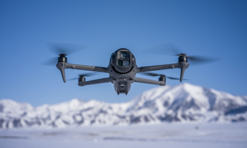 Dron lecący nad zaśnieżonym krajobrazem z górami w tle.