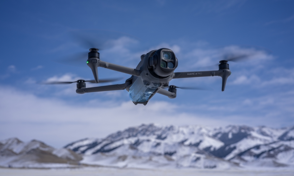 Dron lecący nad ośnieżonymi górami, jasnoniebieskie niebo.