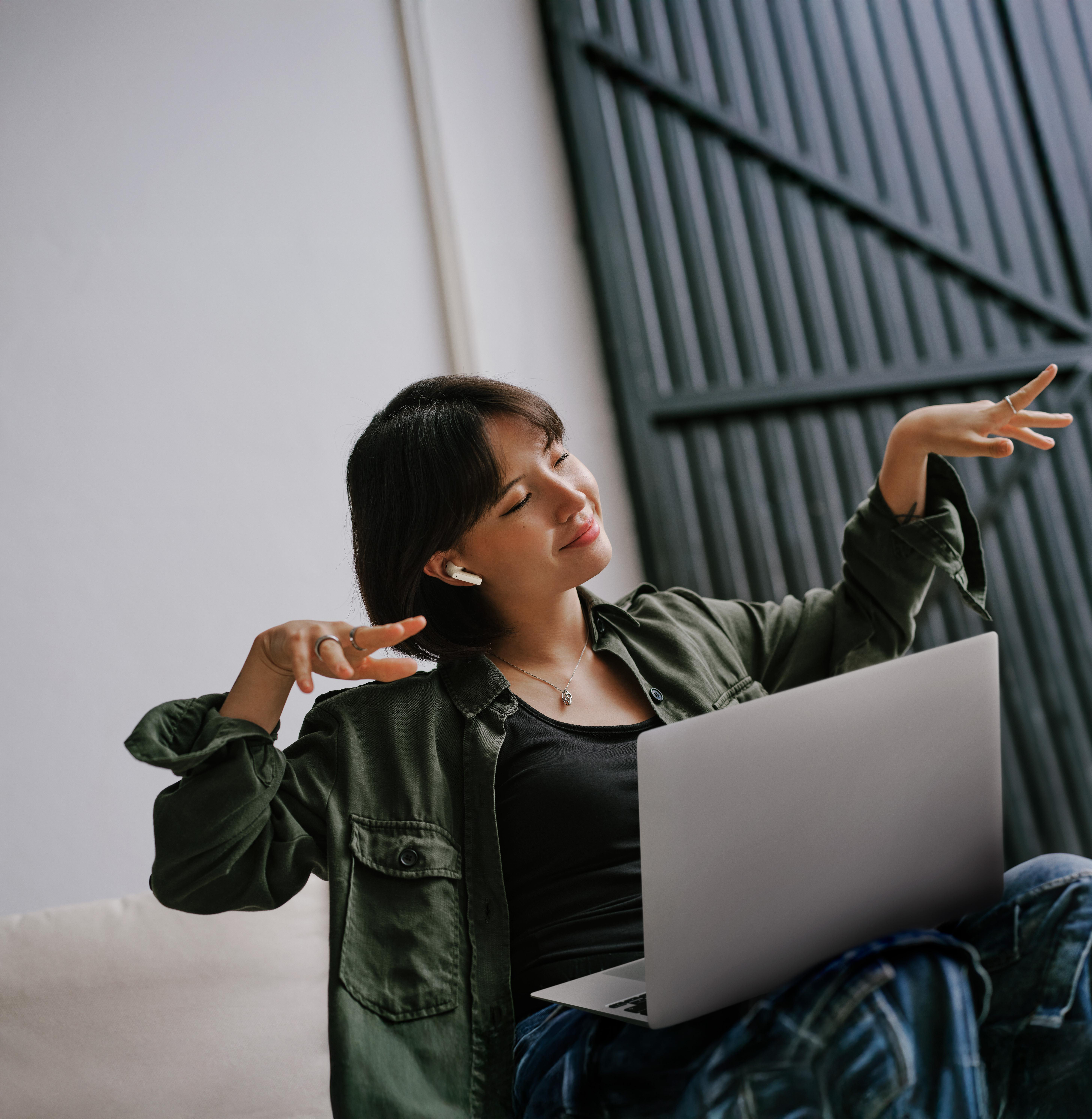 Frau sitzt mit Laptop, trägt Ohrhörer, zeigt Friedenszeichen.
