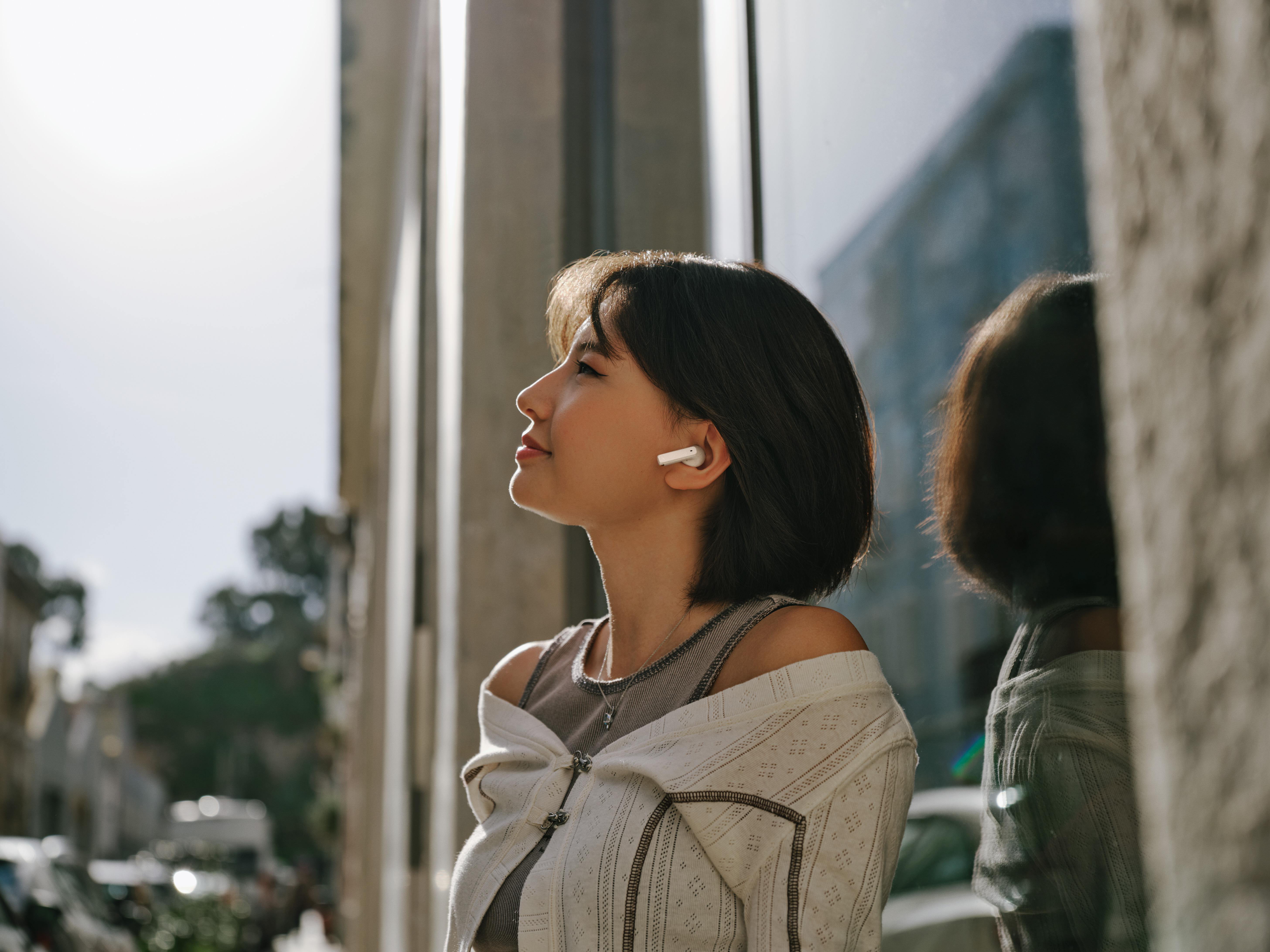 Frau mit Ohrhörern, im Freien, Stadt im Hintergrund, Blick nach oben.