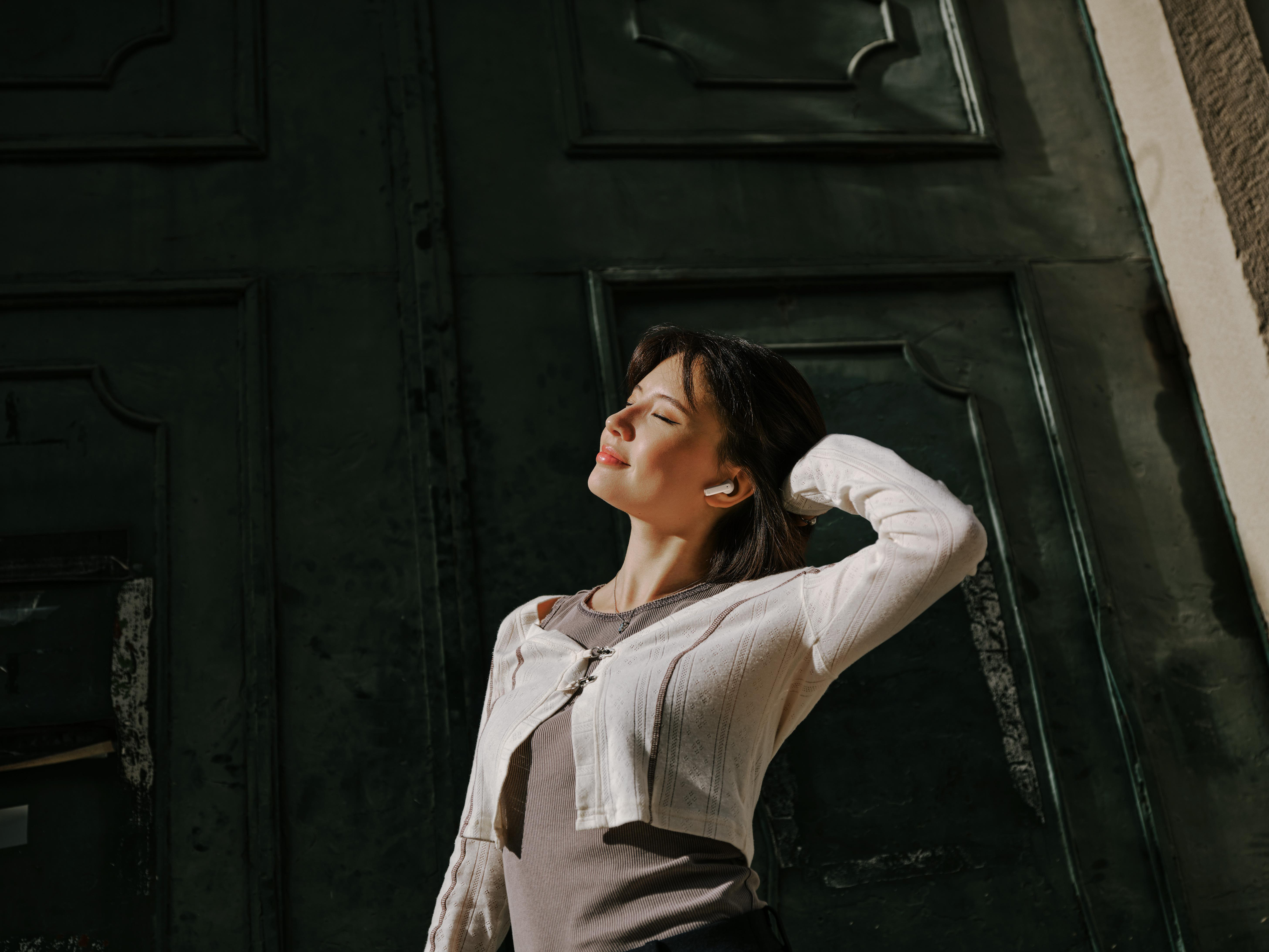 Frau mit Kopfhörern, die im Sonnenlicht steht.