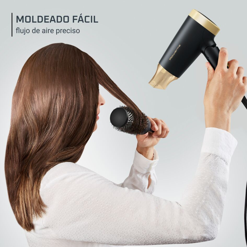 Una mujer se seca el pelo con un secador negro y un cepillo redondo.