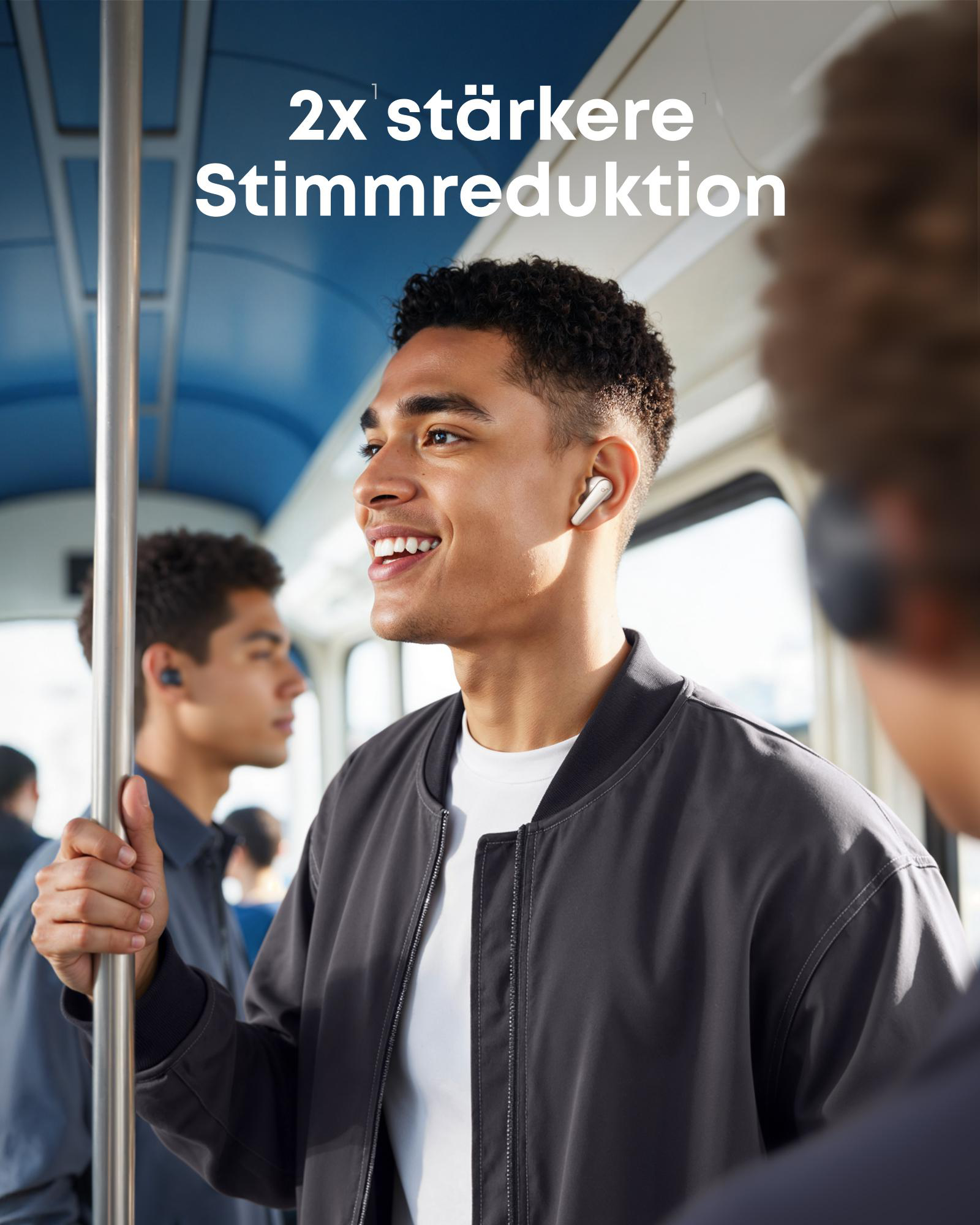 Mann mit Ohrhörern im Zug, lächelt. Hält sich an der Stange fest. Neben ihm steht ein anderer Mann.