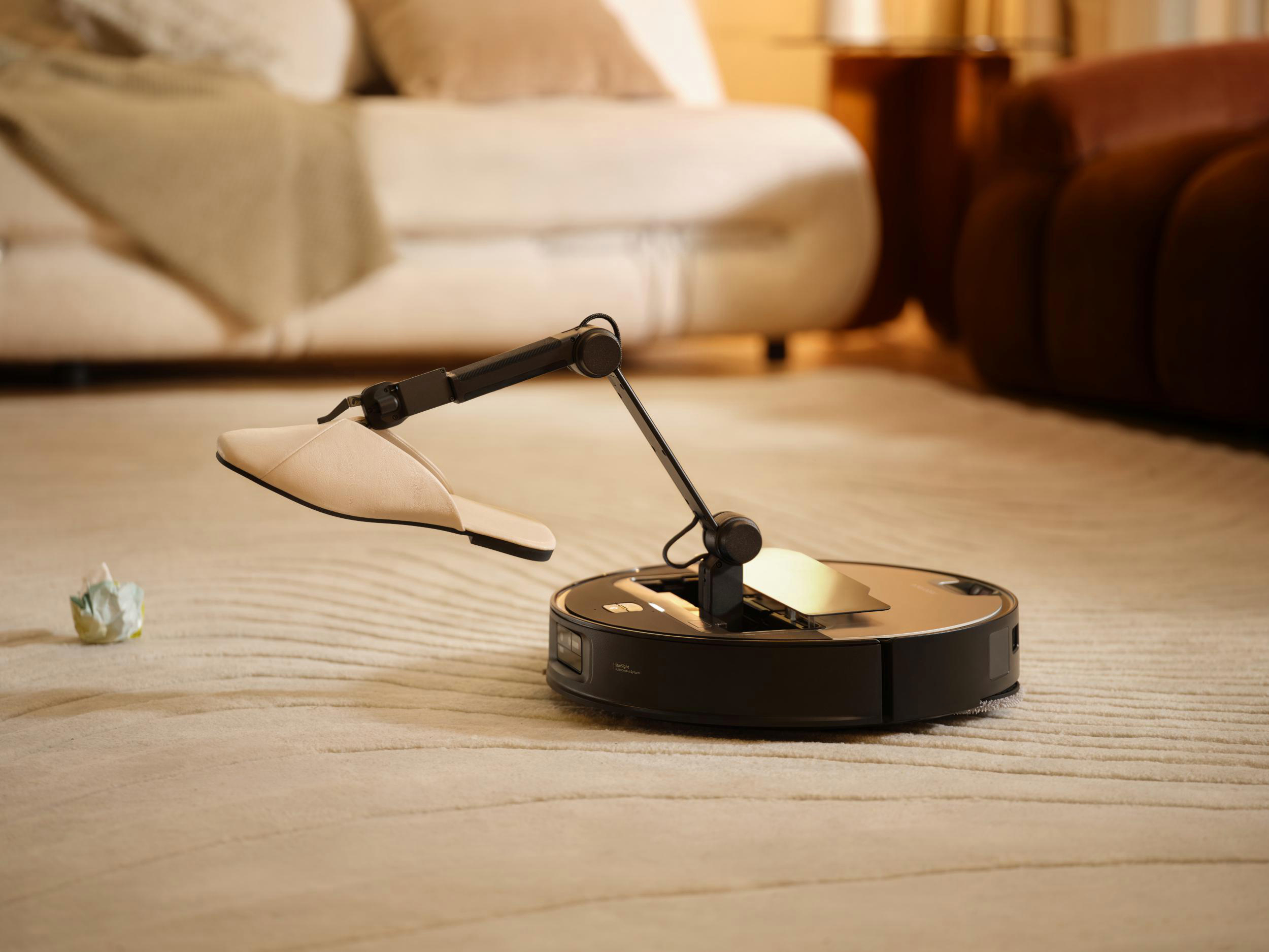 Roboterarm hebt Pantoffel. Hintergrund: Teppich, Möbel.