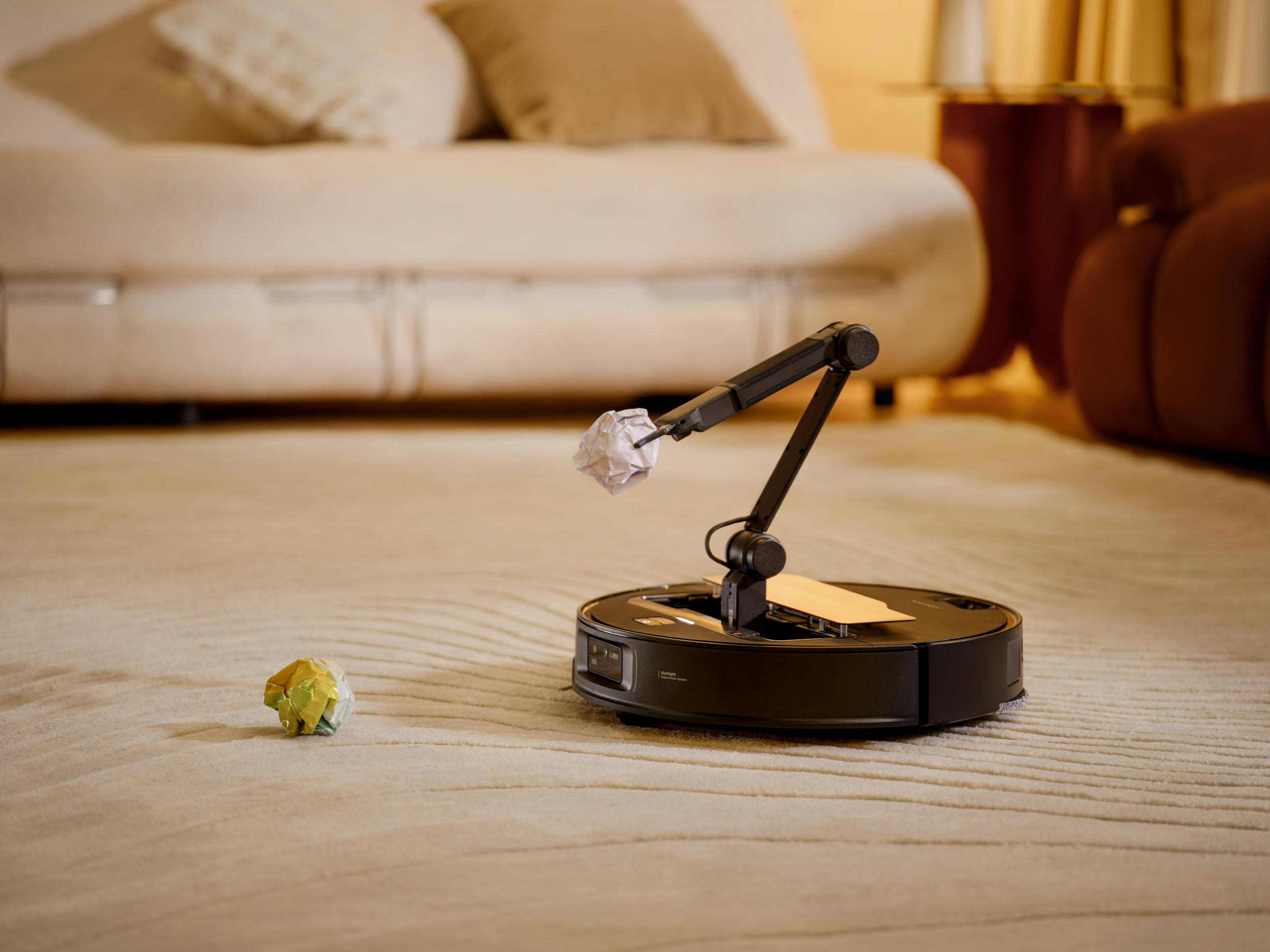 Ein schwarzer Roboter-Staubsauger mit einem Roboterarm, der einen Pantoffel hält, auf einem Teppich.
