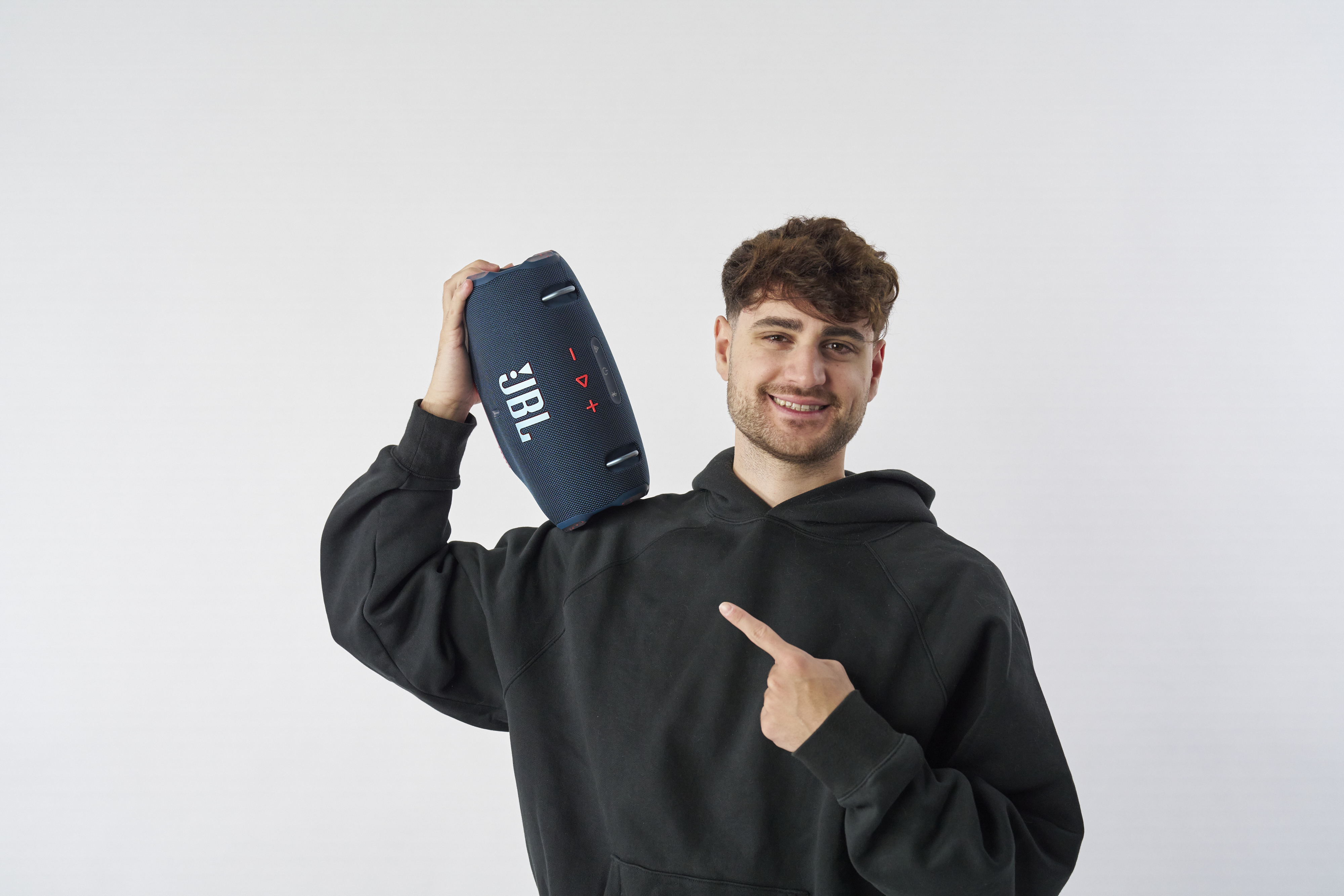 Un uomo tiene un altoparlante JBL blu sulla spalla. Sta indicando l'altoparlante e sorridendo.