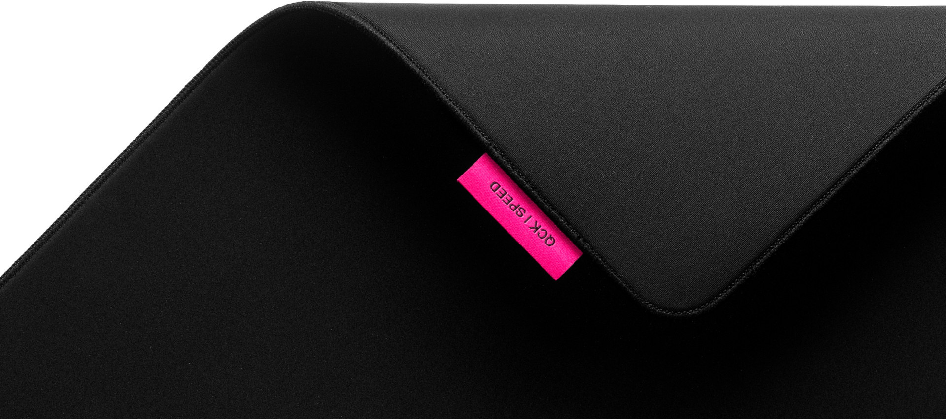 Zbliżenie czarnej podkładki pod mysz z różową etykietą z napisem 'OCK / SPEED'.
