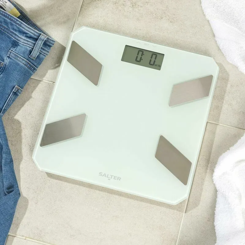 Fehér testmérleg csempézett padlón, farmerrel és törölközővel mellette. 0,0 kg-ot mutat. Salter márka.