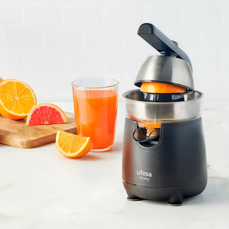 Gyümölcscentrifuga, egy pohár lével töltődik, egy narancs és egy grapefruit szelet mellett.