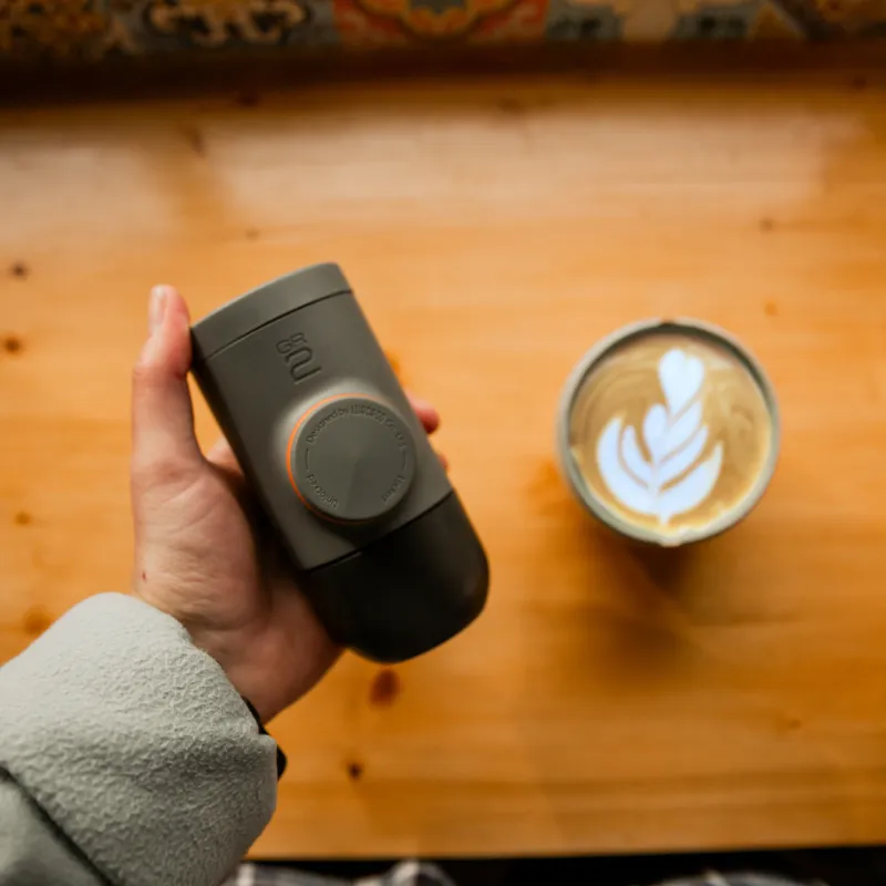 Kézben egy kávéfőző egy latte art-os kávéscsésze mellett.