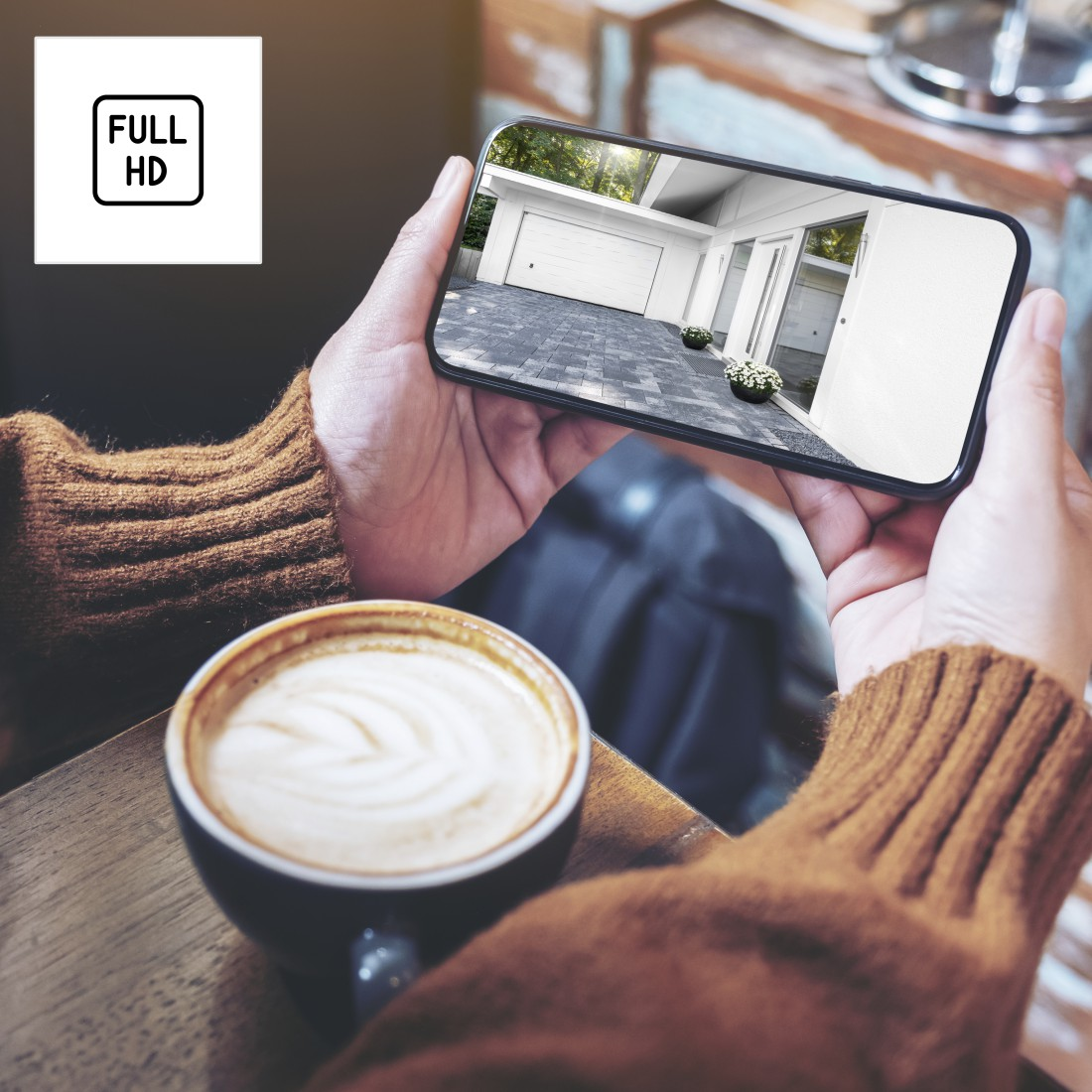 Hände halten ein Smartphone mit einer Garage auf dem Bildschirm. Ein Kaffee steht auf dem Tisch.