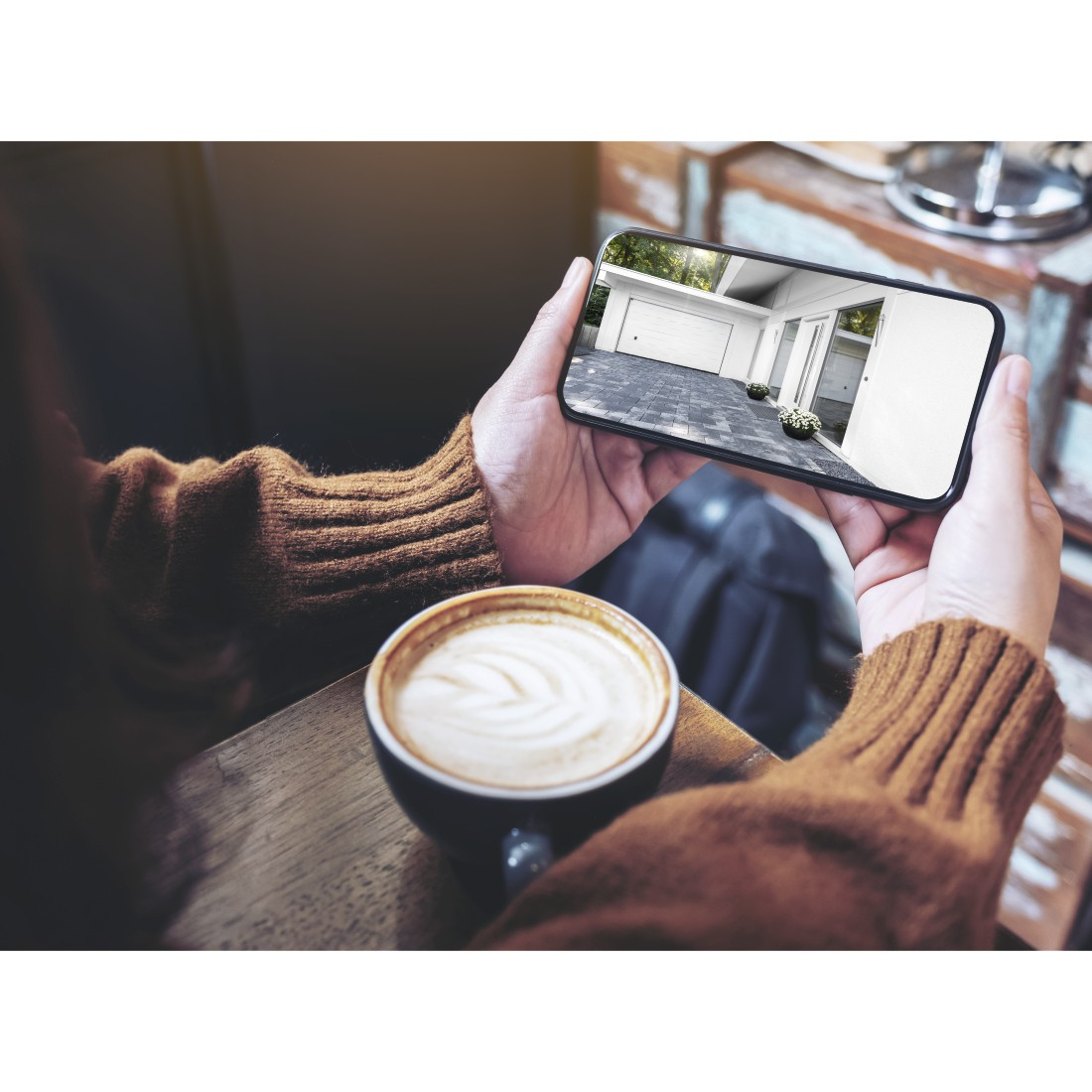 Hände halten ein Smartphone mit einem Garagenbildschirm. Ein Kaffee steht auf dem Tisch.