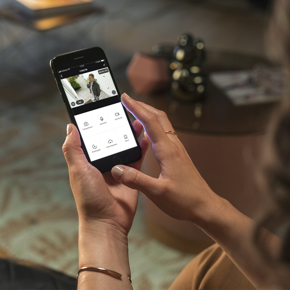 Hände halten ein Smartphone, auf dem eine Überwachungskamera-Ansicht zu sehen ist.