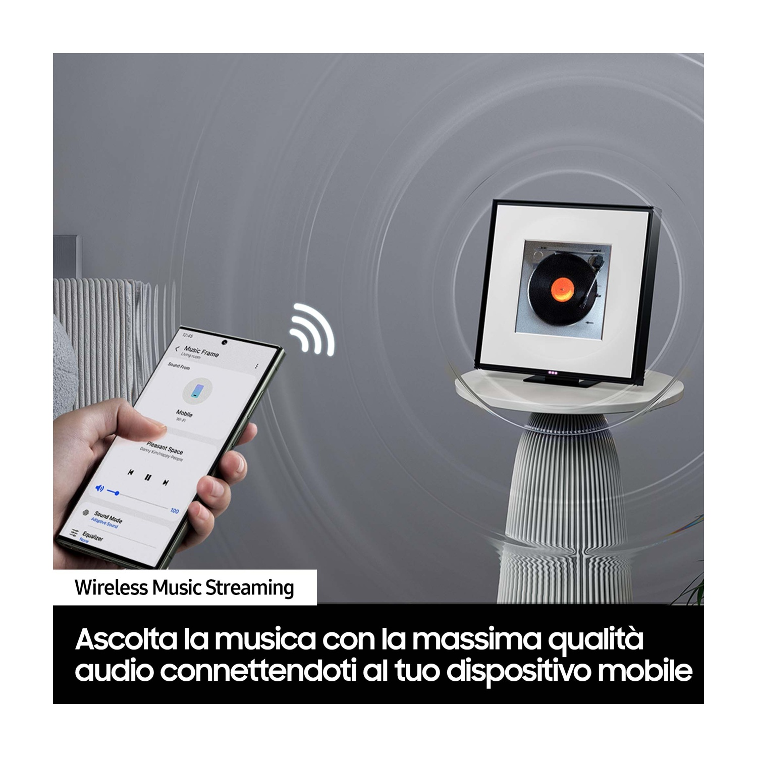 Persona che tiene in mano uno smartphone con app musicale, accanto a un altoparlante con cornice nera su piedistallo.