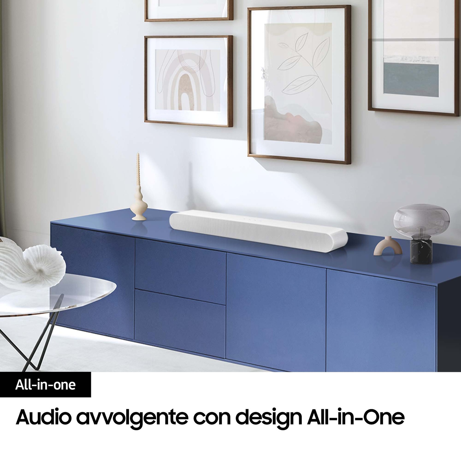 Una soundbar bianca su un mobile blu. Quadri appesi sullo sfondo.