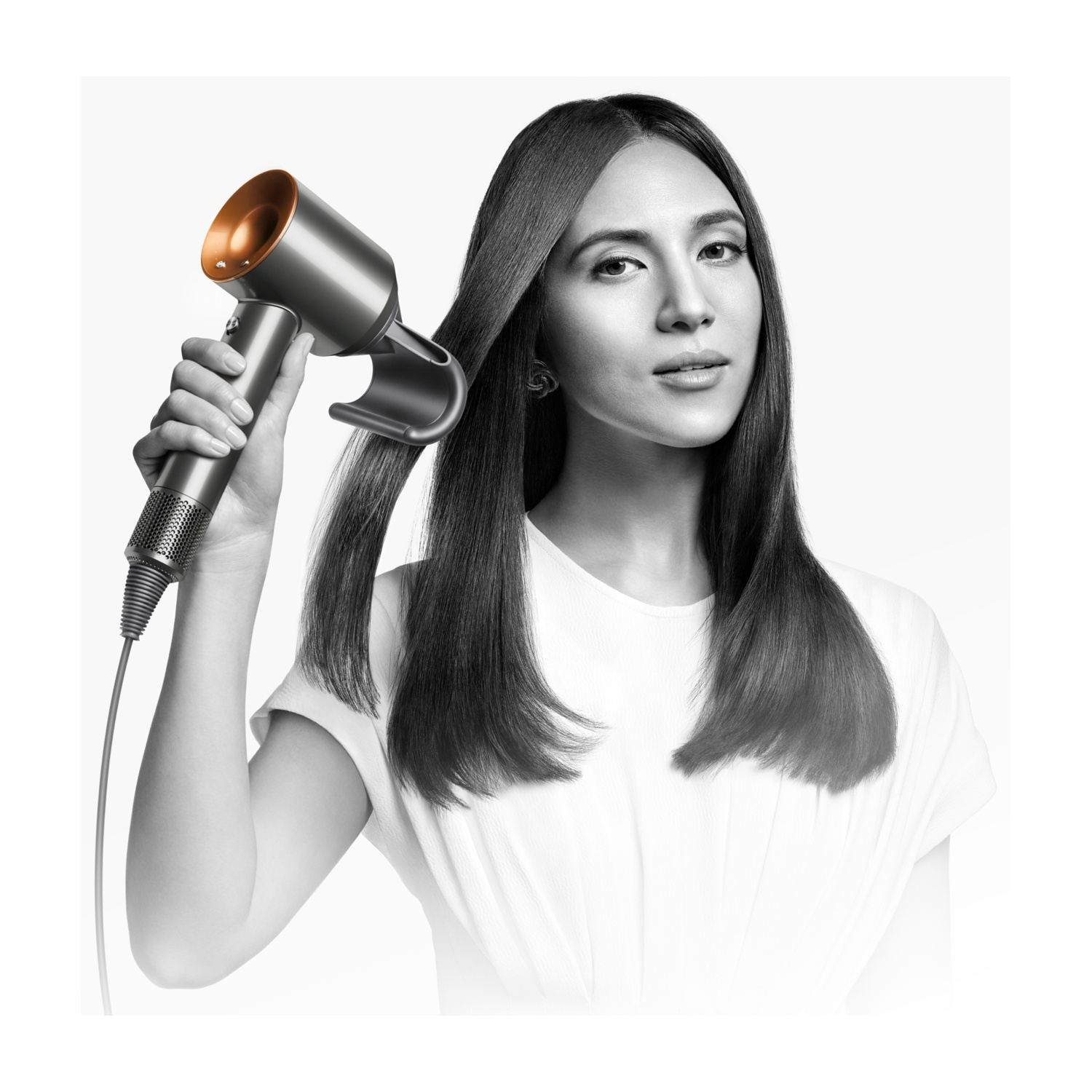 Una donna che si sistema i capelli con un asciugacapelli, su sfondo bianco.