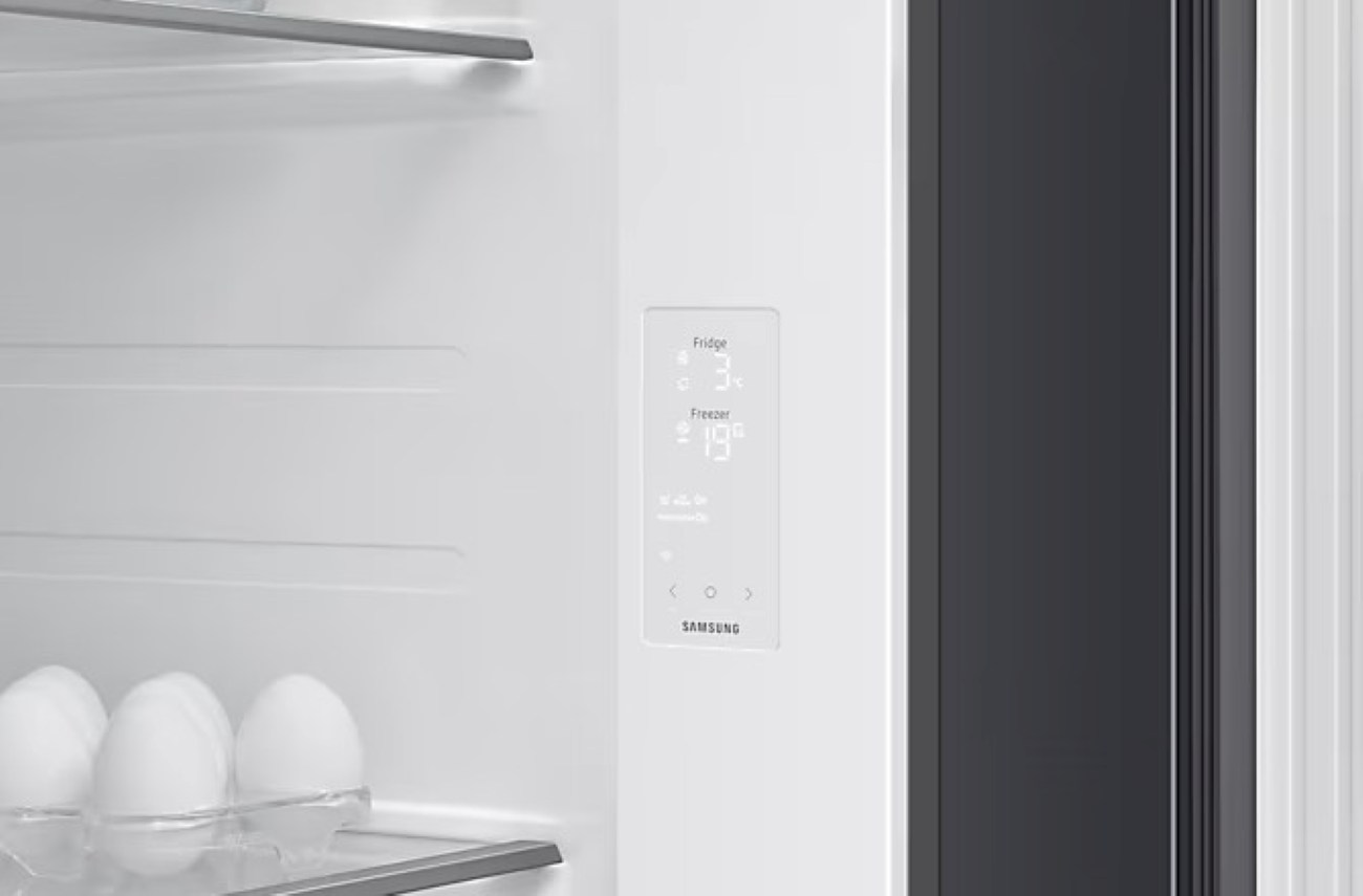Wewnątrz lodówki panel cyfrowy pokazuje 3°C dla lodówki i 19°C dla zamrażarki. Na półce widać jajka.
