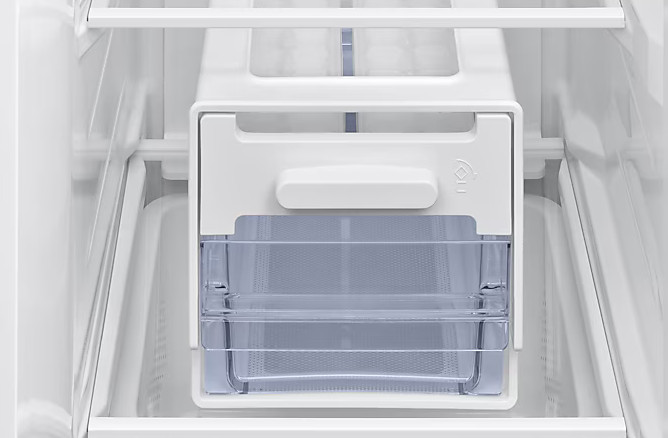 Wewnątrz białej lodówki. Widoczny biały automat do lodu i przezroczyste szuflady. Wnętrze ma białe półki i ściany.