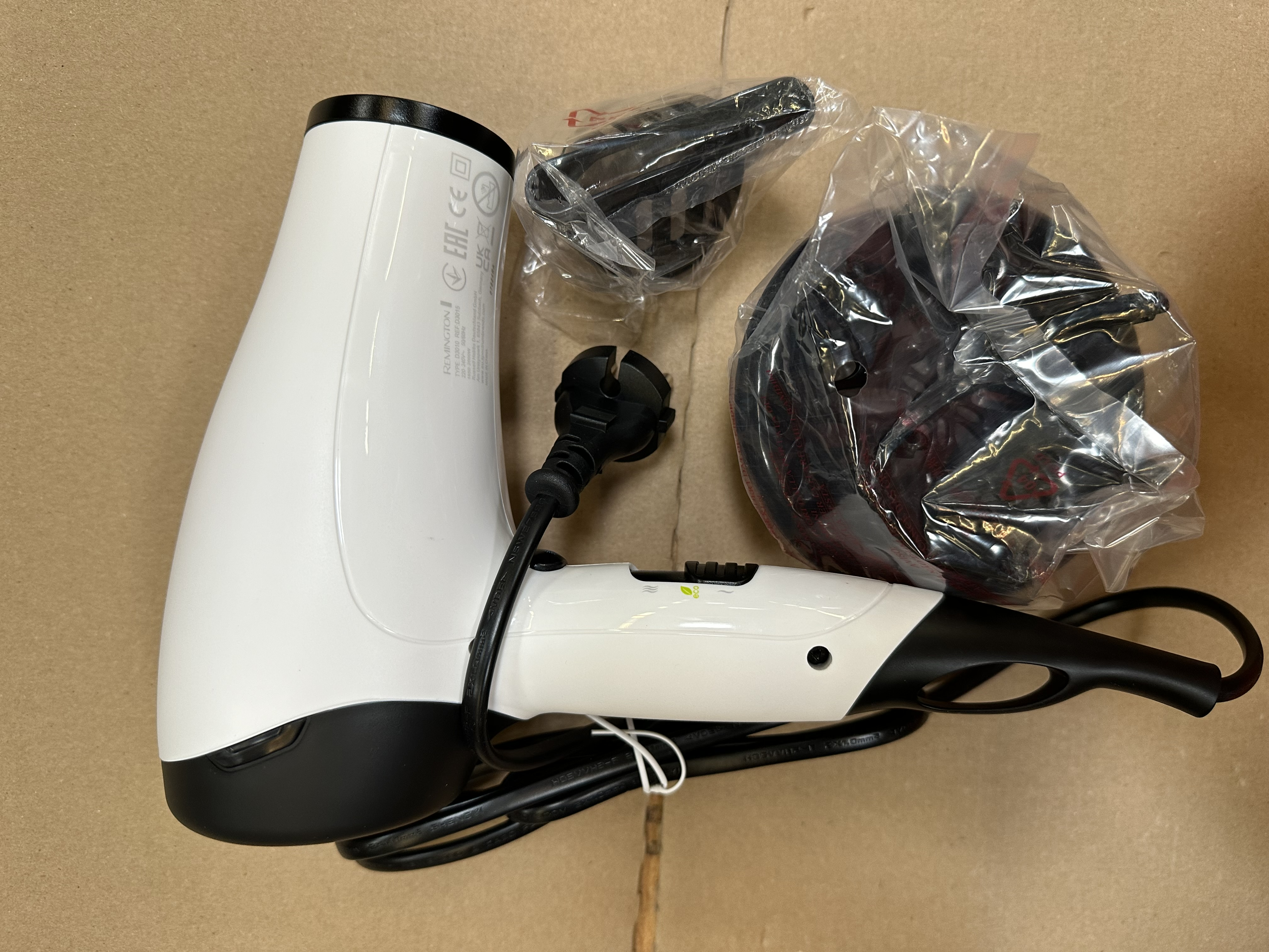 Biała suszarka do włosów z czarnym uchwytem i kablem, obok akcesoria w plastiku.