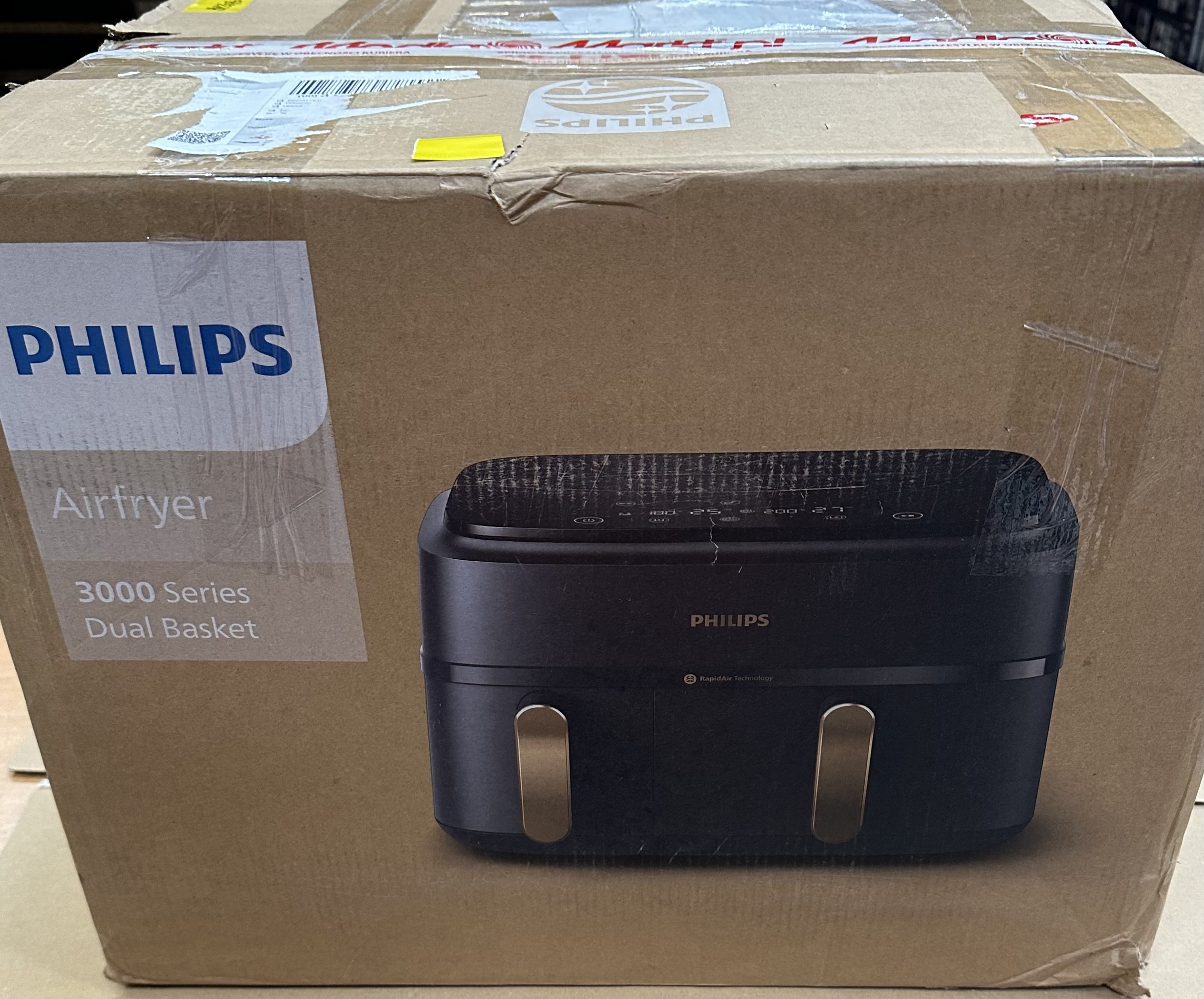 Pudełko Philips Airfryer pokazujące czarną frytkownicę z złotymi uchwytami, wewnątrz kartonowego pudełka.