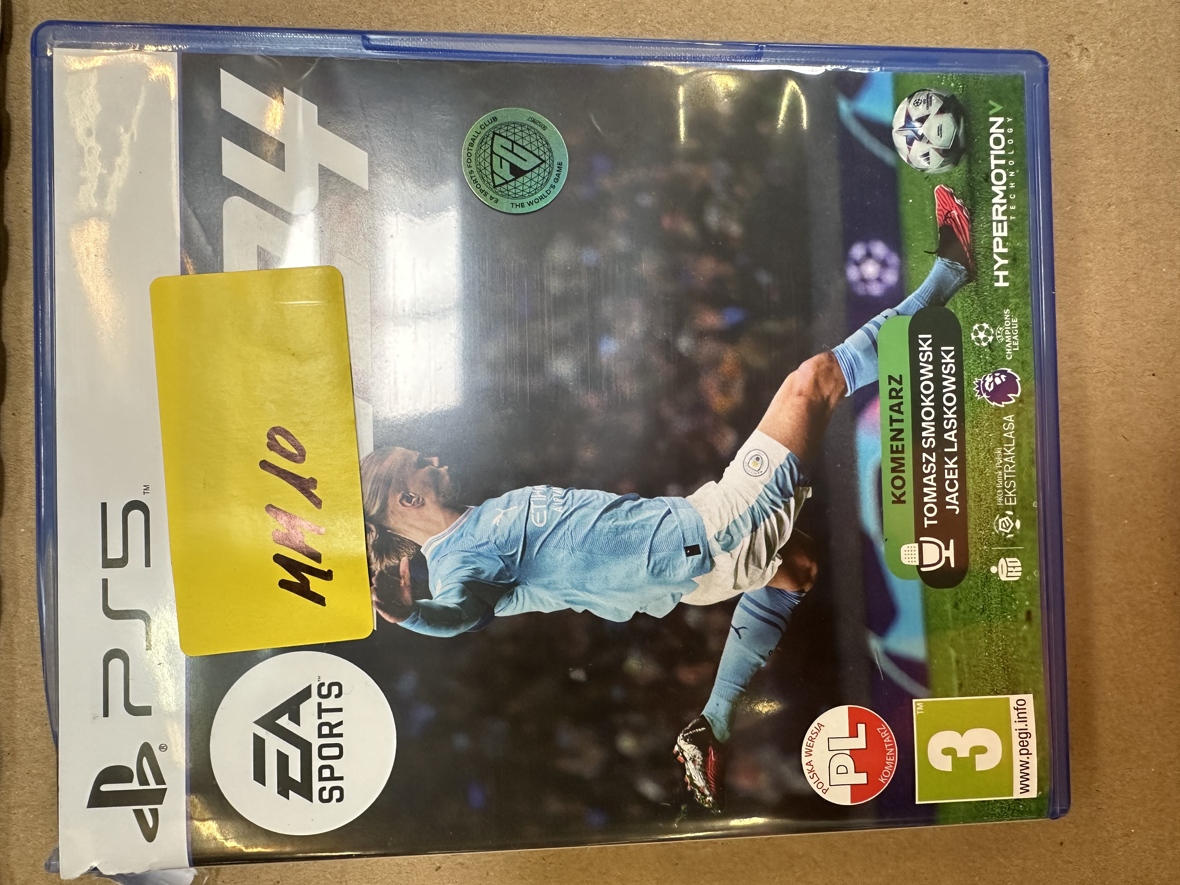 Pudełko z grą wideo z FC24. Obraz gracza, logo PS5, klasyfikacja wiekowa. Żółta naklejka.