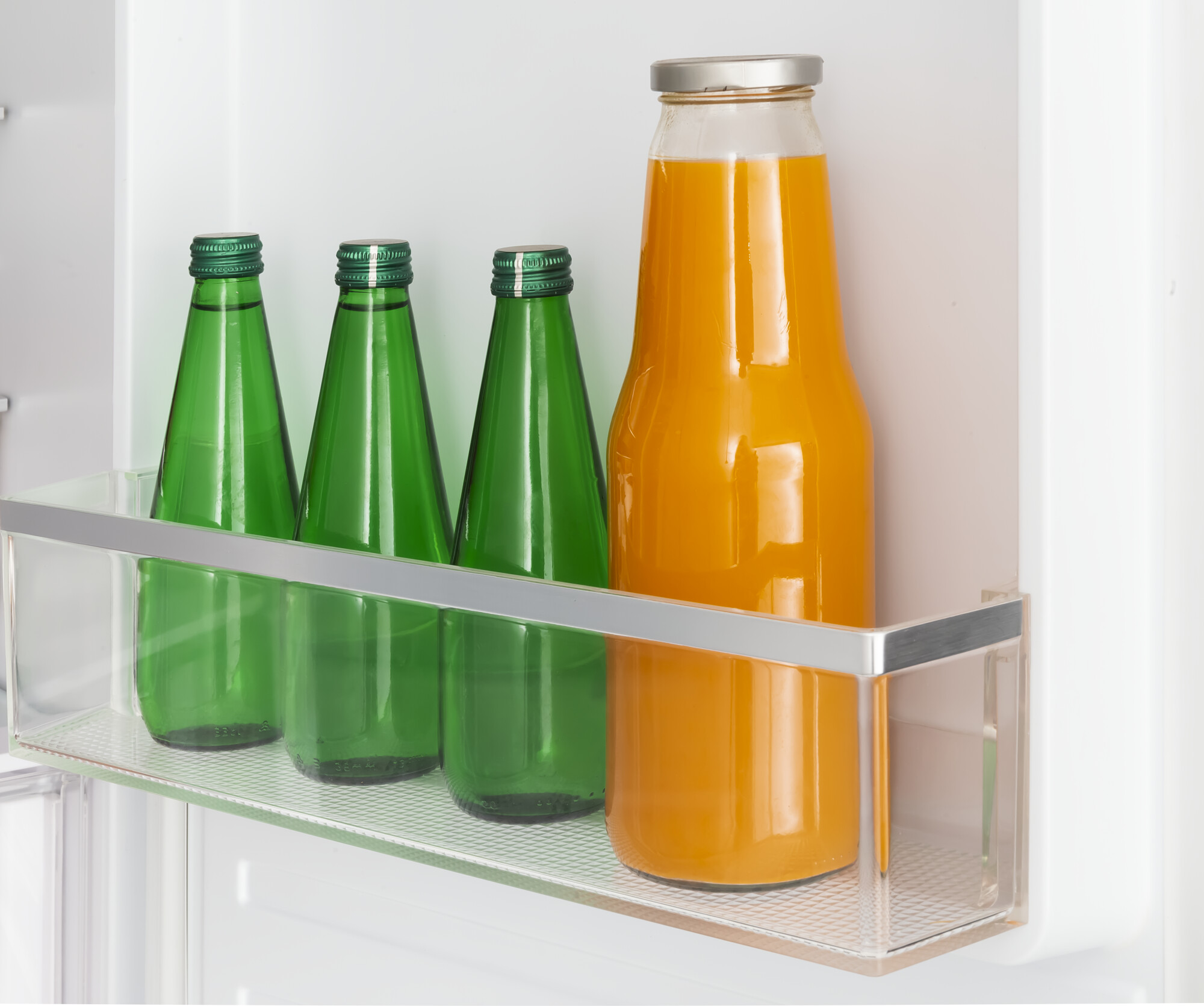 Im Kühlschrank stehen drei grüne Flaschen und eine große Flasche mit Orangensaft in einem Fach.