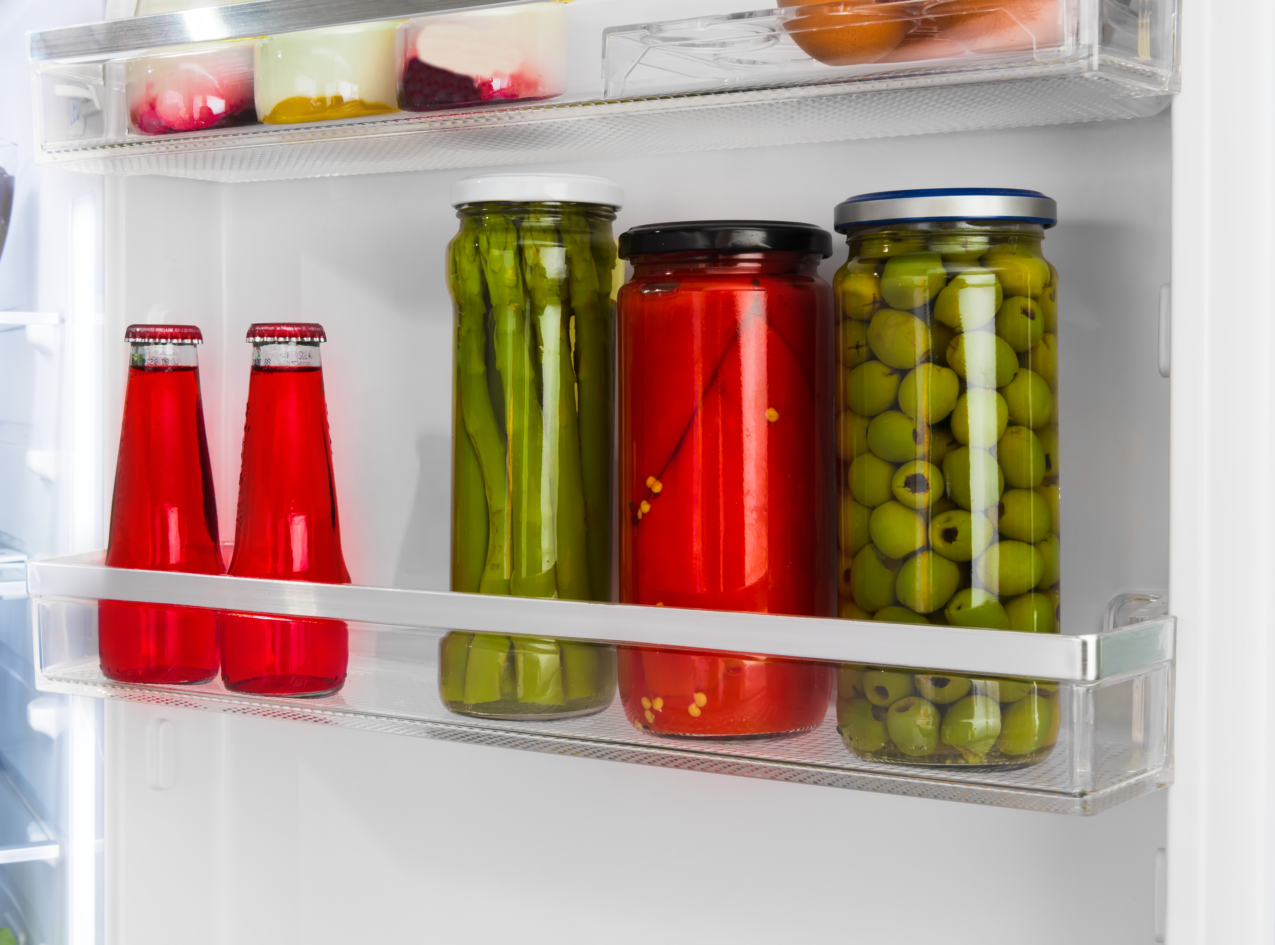 Im Kühlschrank stehen zwei rote Getränkeflaschen und Gläser mit eingelegten Lebensmitteln.