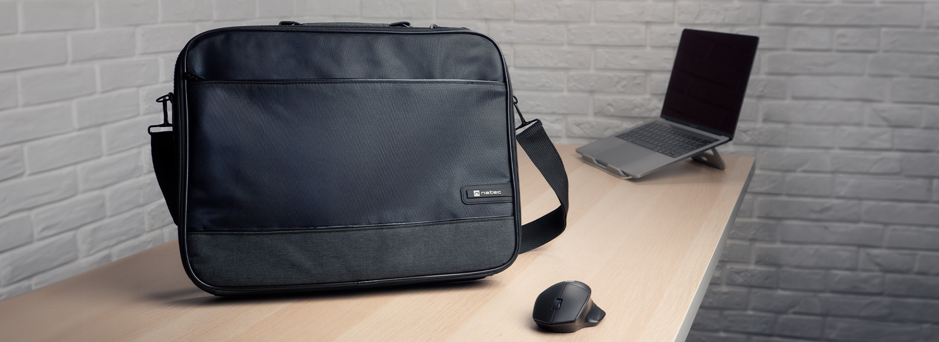 Egy fekete laptop táska és egy laptop az asztalon. Egy állvány és egy egér is látható.