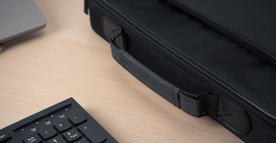 Fekete aktatáska fogantyúval és cipzárral egy faasztalon, mellette billentyűzet és laptop.