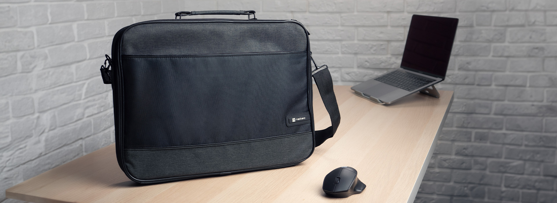Fekete laptop táska egy faasztalon, mellette egy laptop állványon és egy egér.