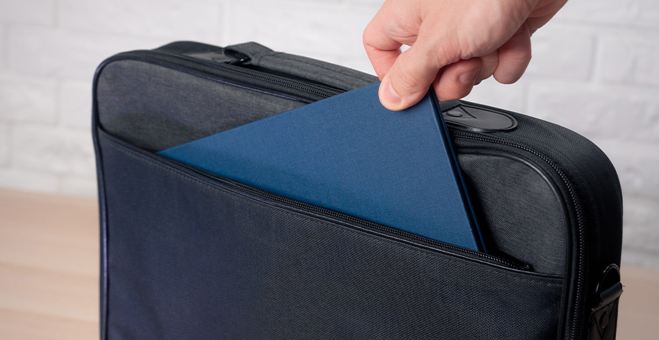 Kéz kék mappát helyez egy fekete laptop táskába.