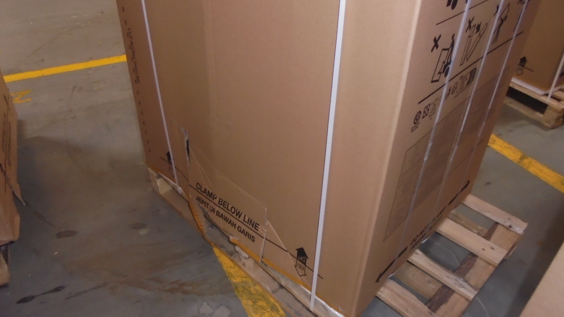 Karton na palecie. Tekst na pudełku: 'Clamp below line'. Środowisko magazynowe.