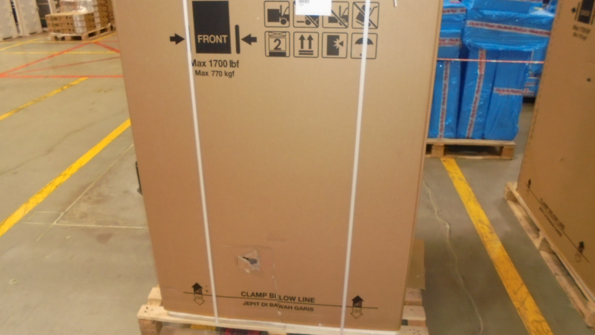 Duże kartonowe pudełko na drewnianej palecie. Tekst w języku angielskim i indonezyjskim.