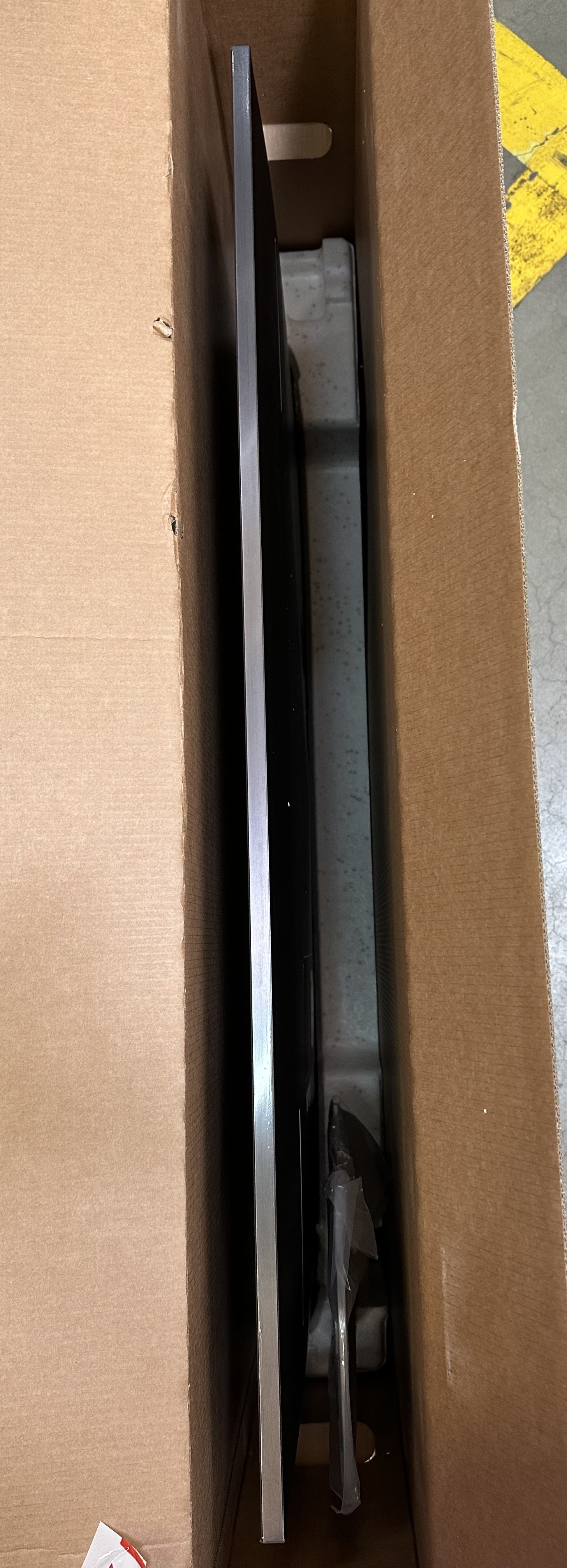 Wewnątrz kartonowego pudełka: ekran telewizora w ramie, z ochronnym opakowaniem.