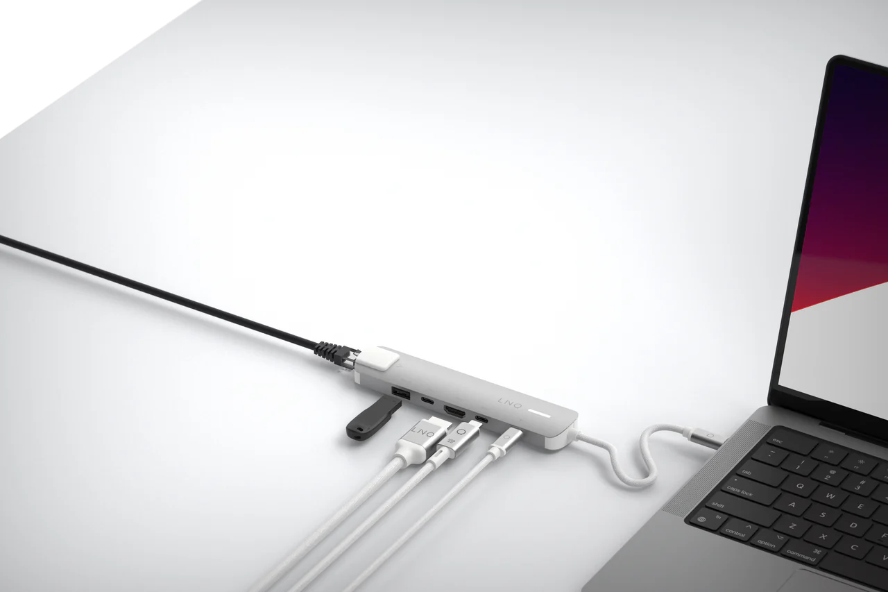 Un portátil conectado a un concentrador USB-C con múltiples cables blancos. Mesa blanca.