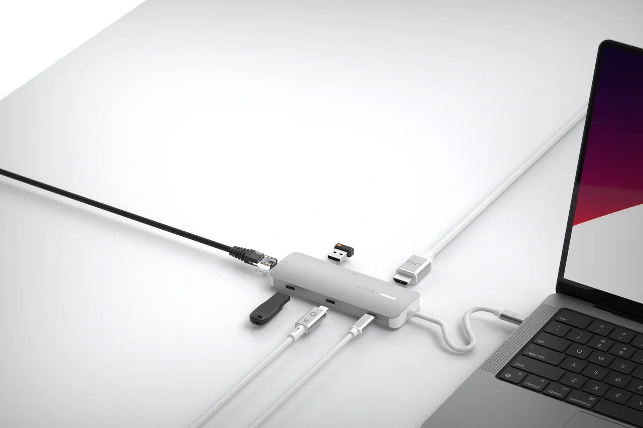Un concentrador USB-C con varios puertos conectado a un portátil sobre una superficie blanca.