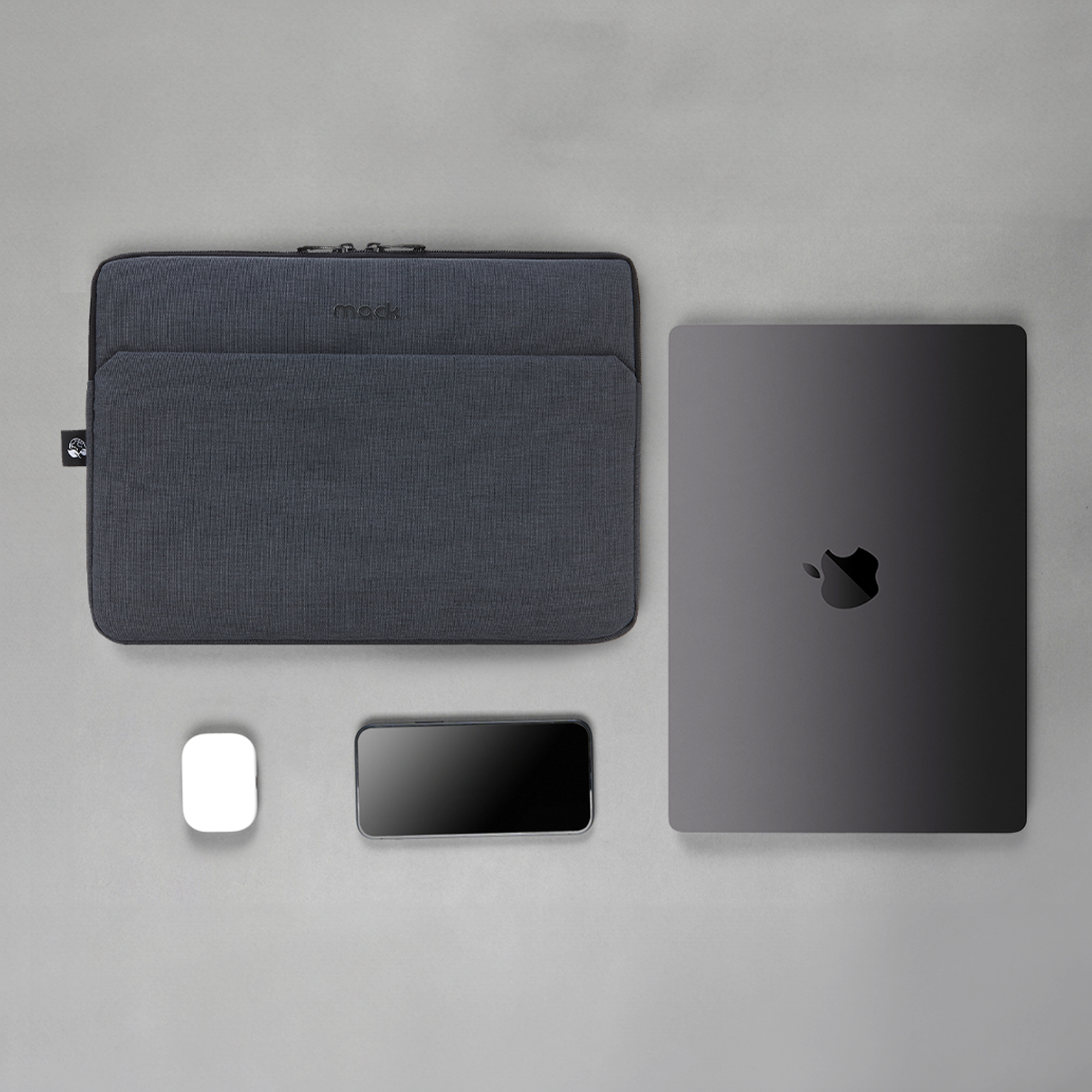 Gri laptop kılıfı, bir laptop, telefon ve beyaz bir cihaz ile gri bir yüzey üzerinde.