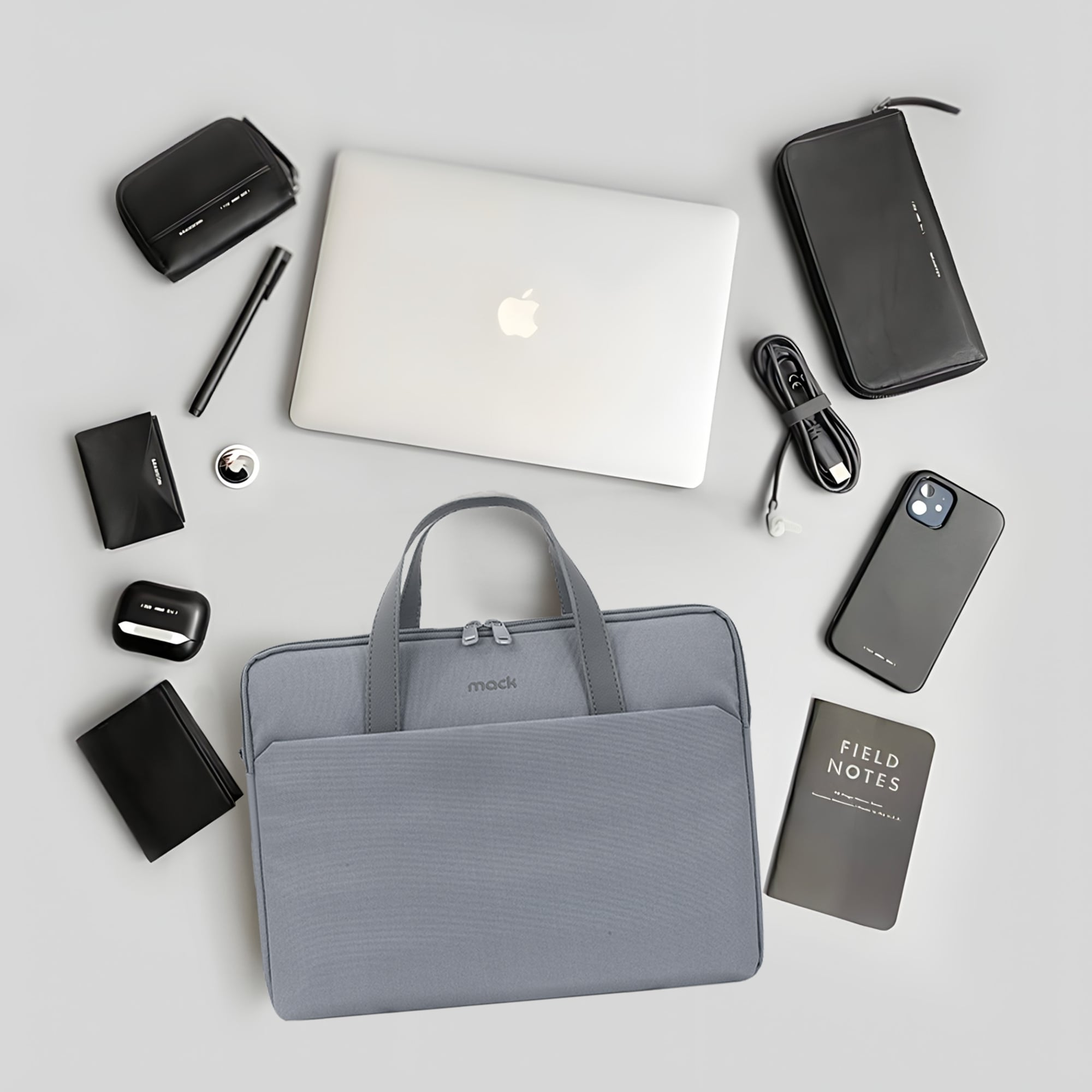 Gri Mack laptop çantası, etrafında laptop, telefon ve aksesuarlar dahil olmak üzere çoklu eşyalarla.