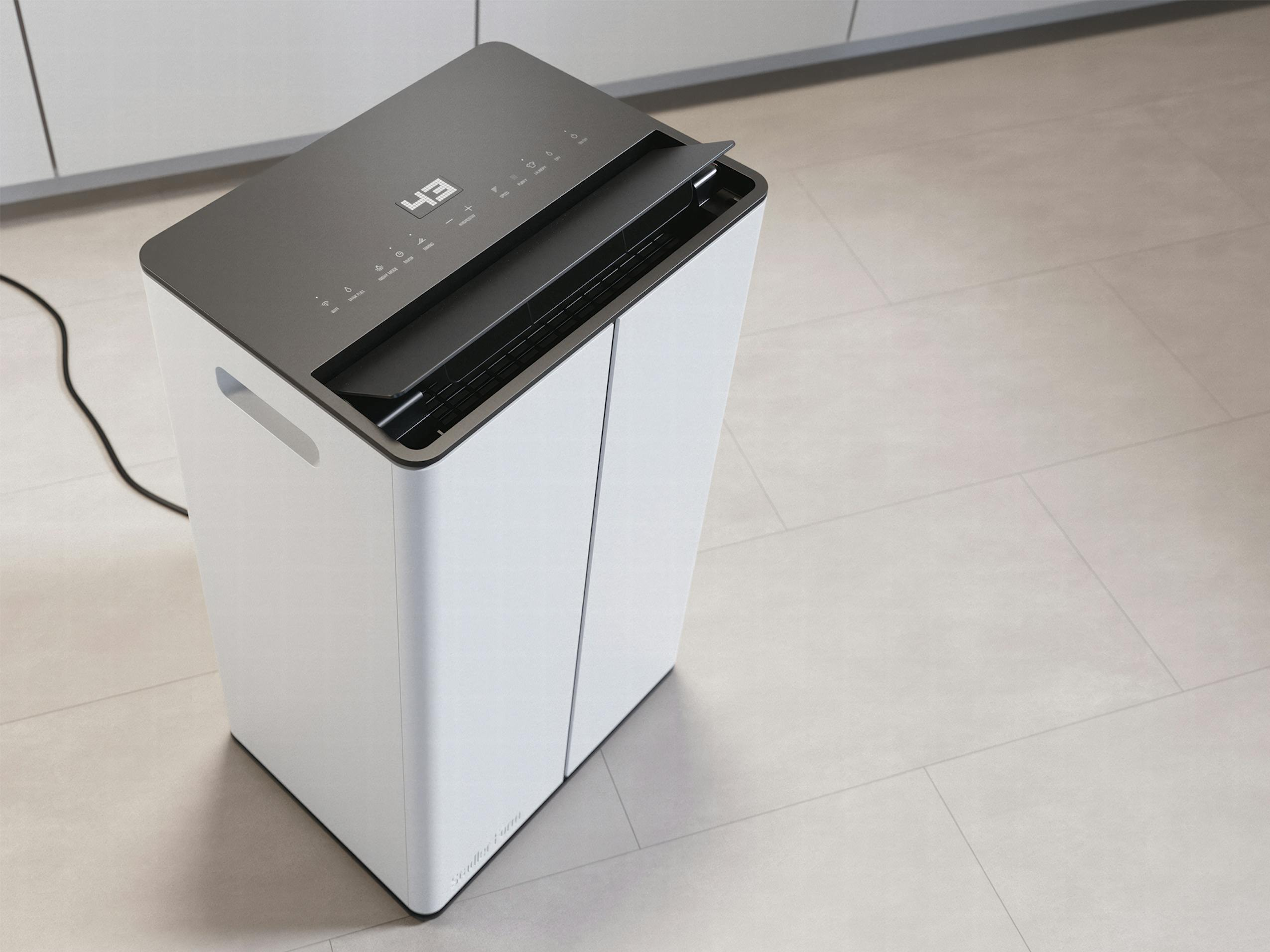 Purificatore d'aria bianco con top nero. Display mostra '43'. Posizionato su pavimento chiaro.